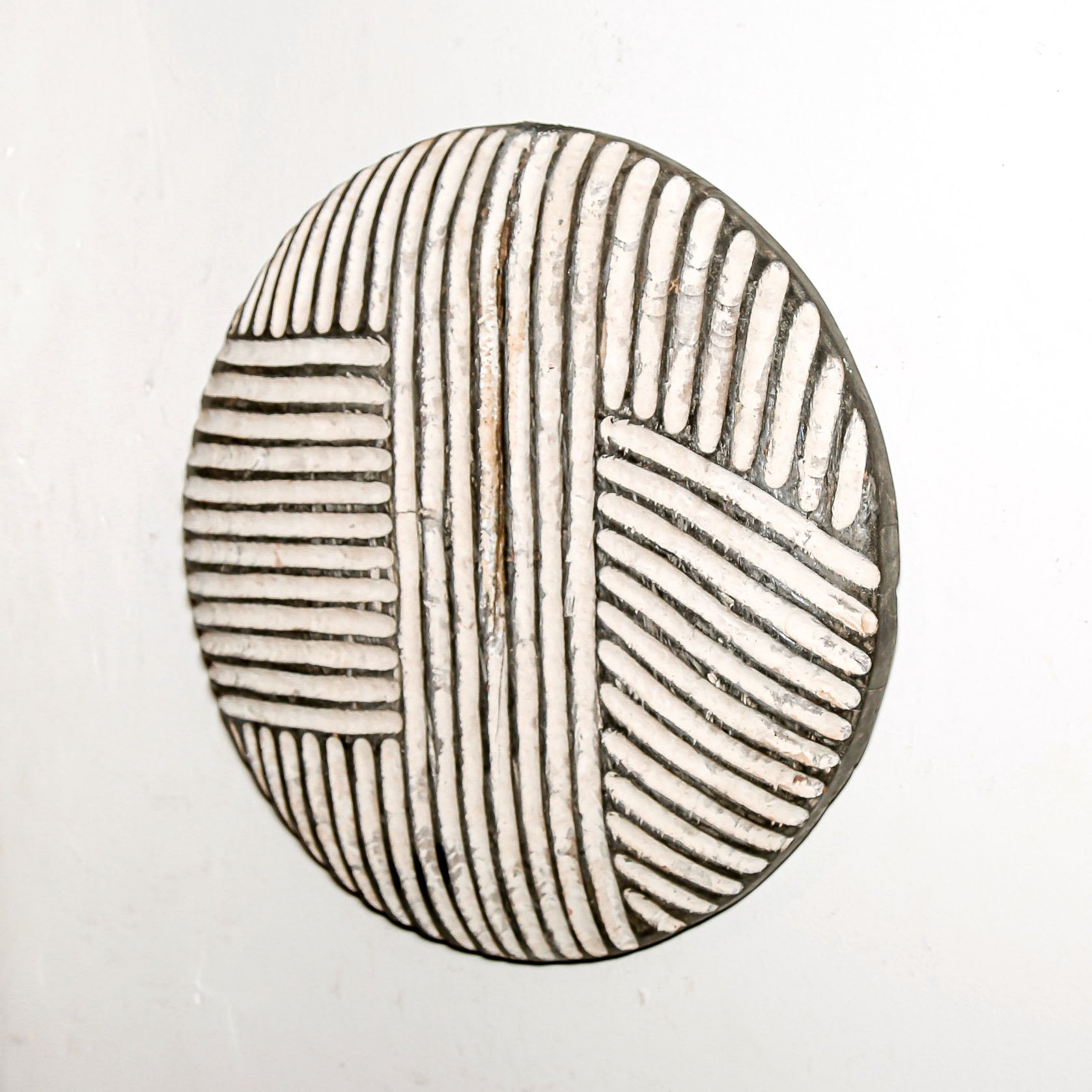 Round wood wall decor with rustic African traditional striped pattern on a white living room wall