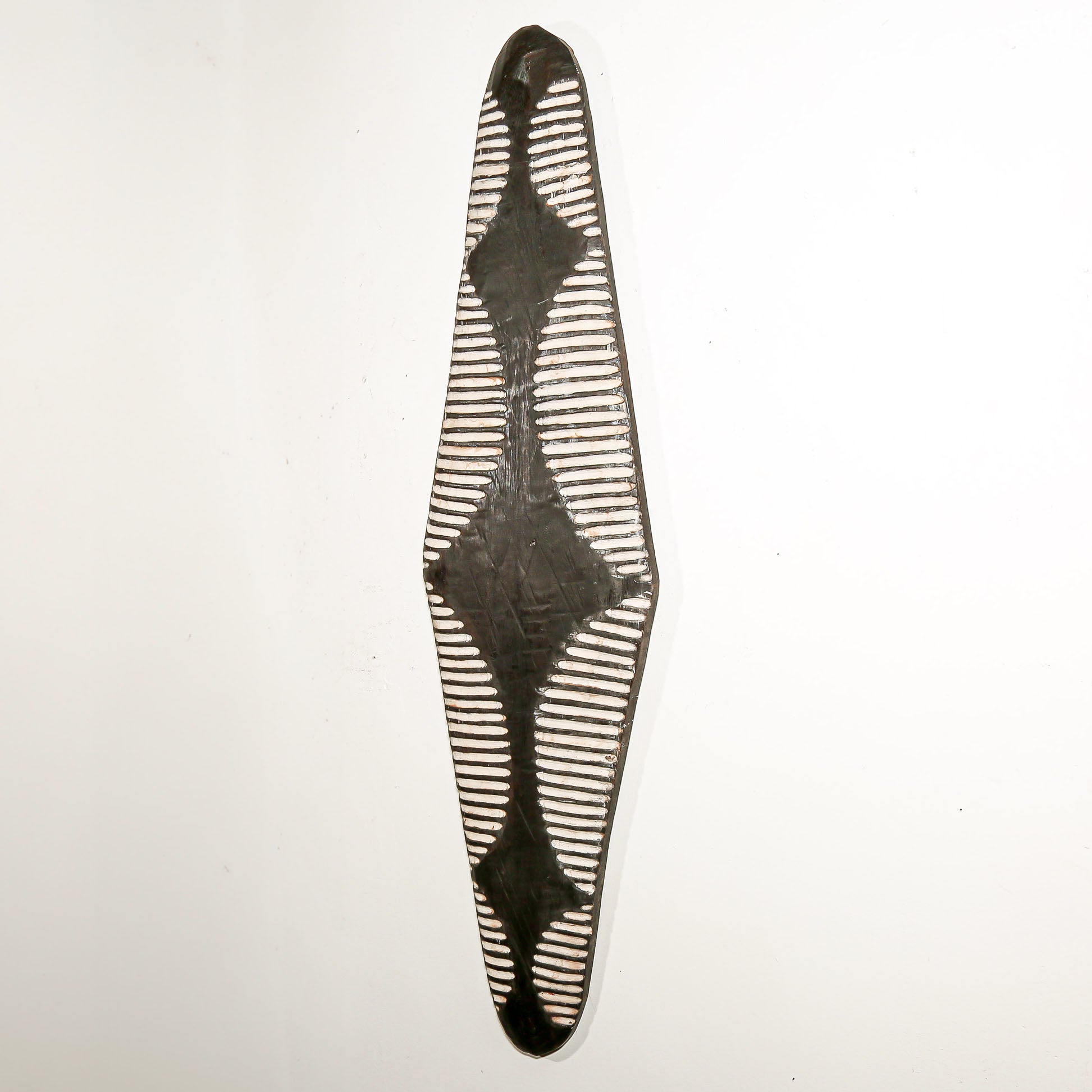 Long wood wall decor with rustic African traditional striped pattern on a white living room wall