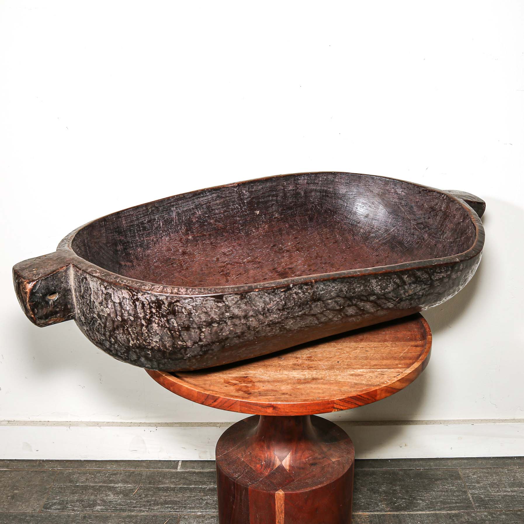 Decorative wooden vintage African oval bowl on a stand against a white wall