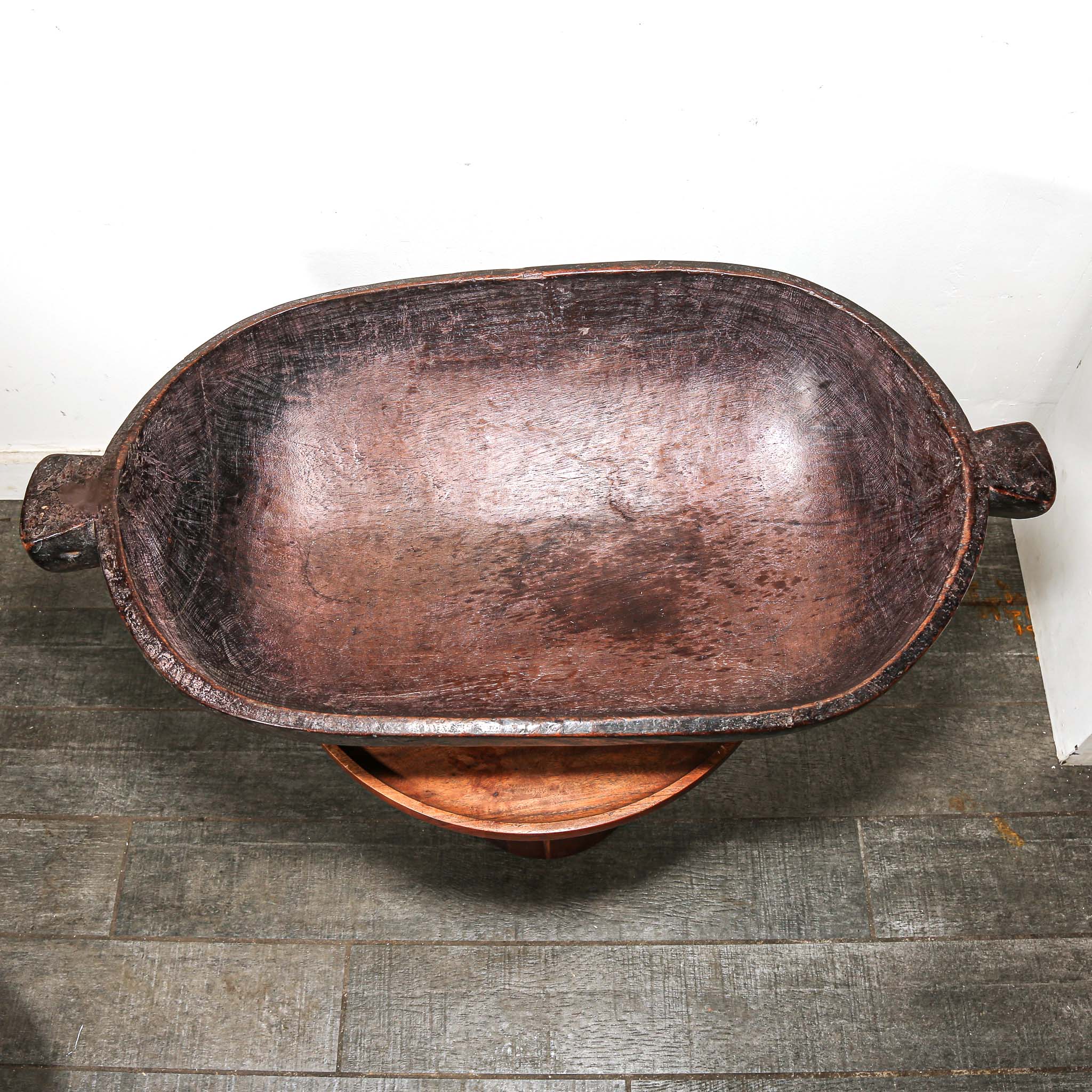Decorative wooden vintage African oval bowl on a stand against a white wall