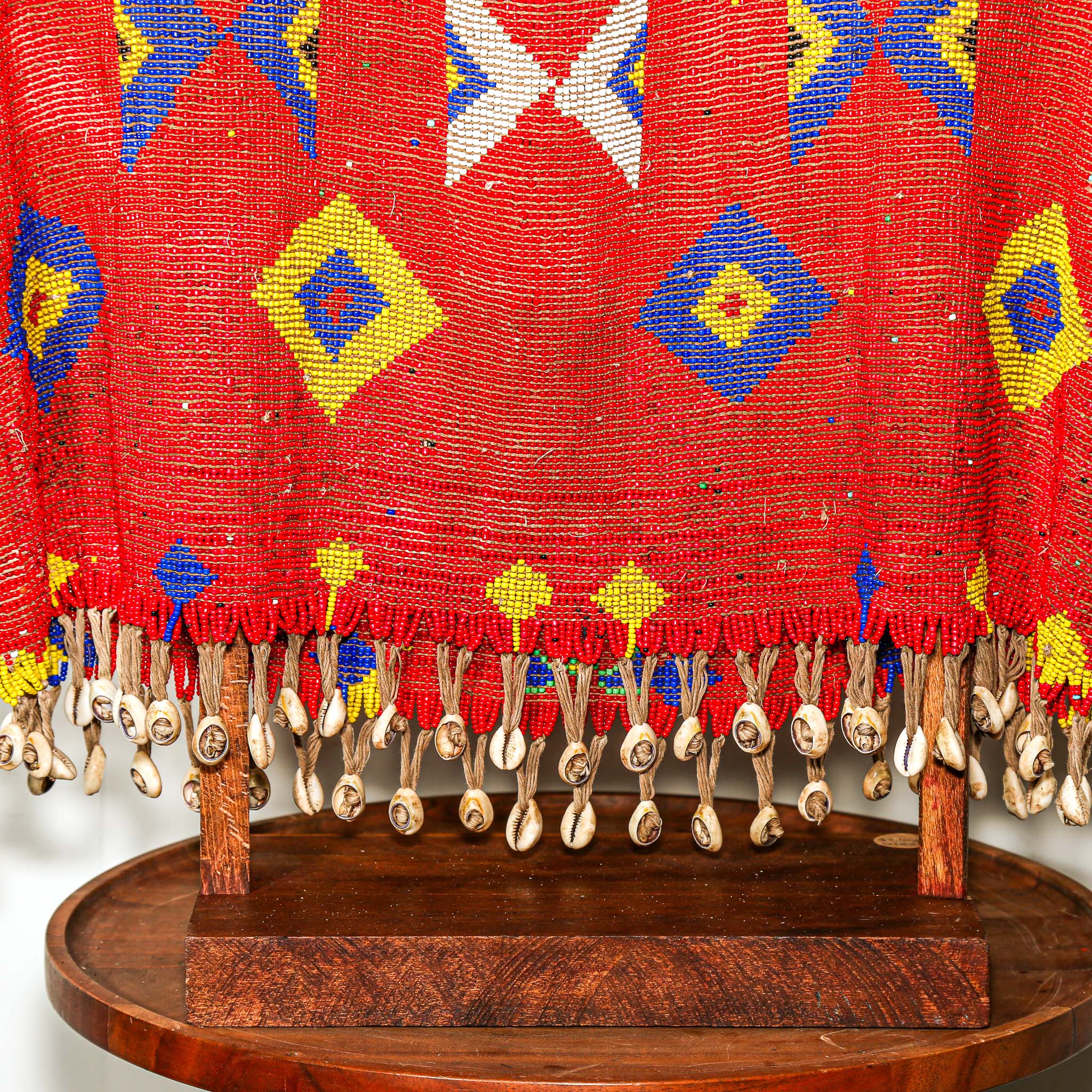 Red beaded garment for sculptural display with geometric patterns on a stand against a white background. high quality collectable African art