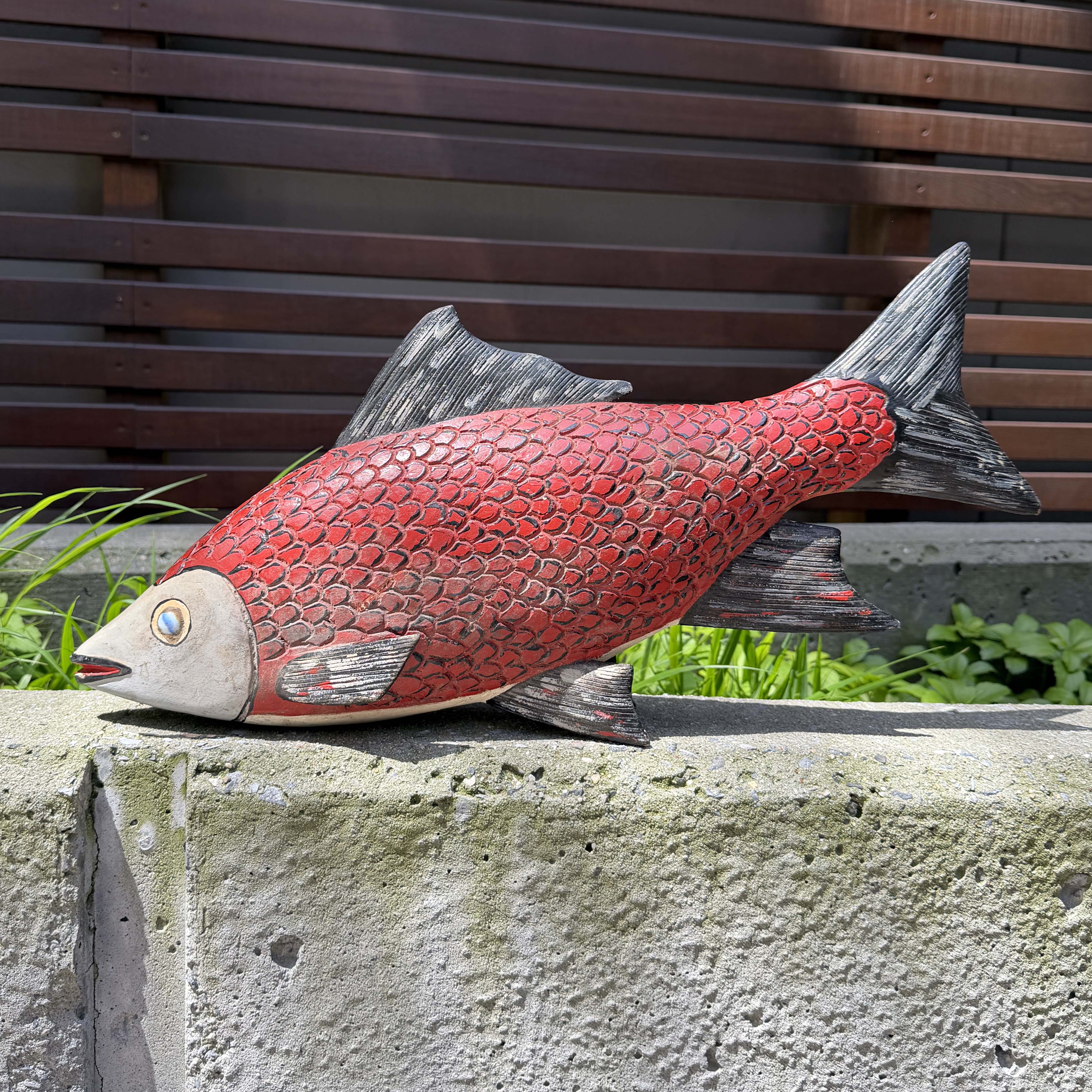 Red fish sculpture on a stone ledge with a wooden background