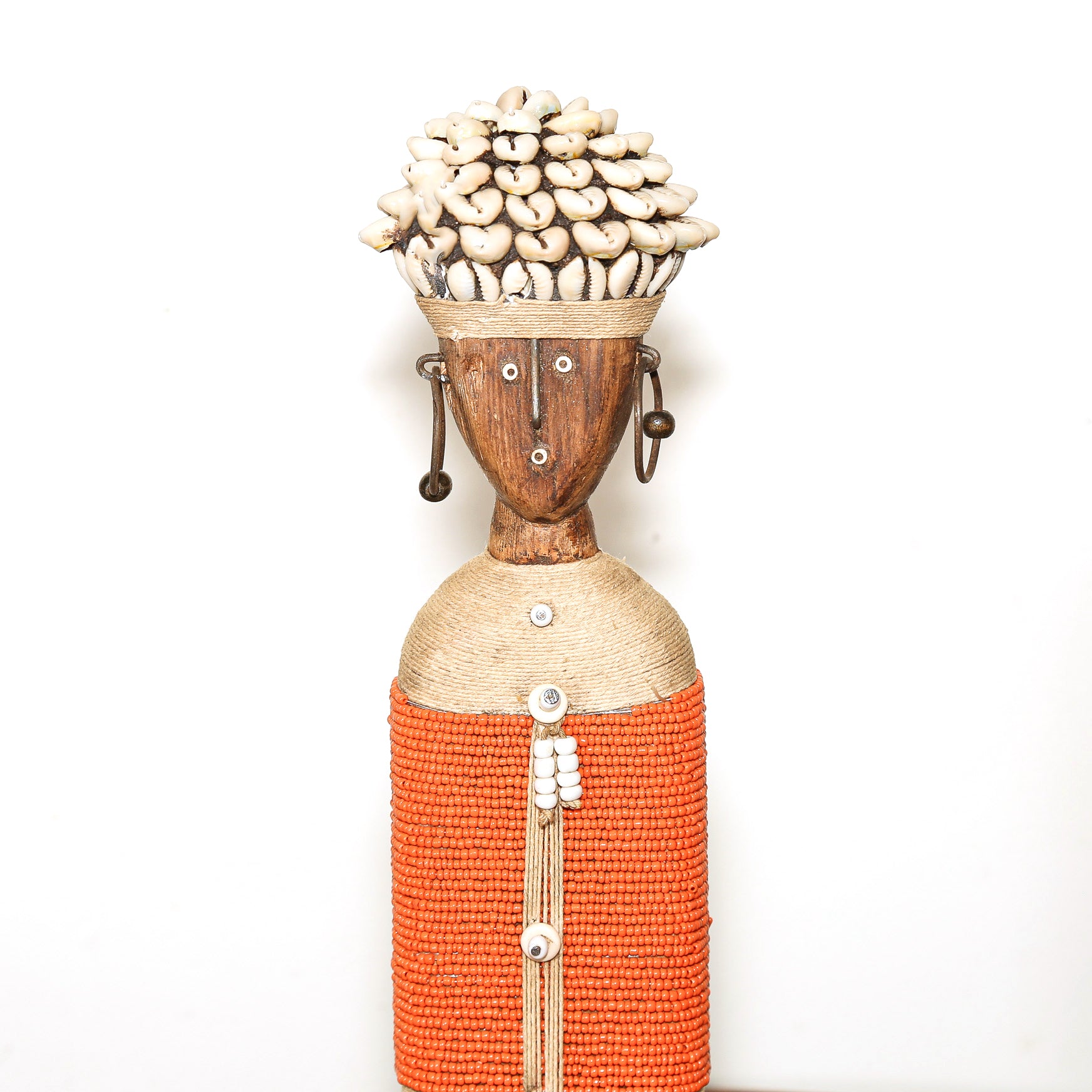 A handmade African-style wooden doll sculpture with a brown face, white shell hair, and an orange beaded dress, set against a plain white background.