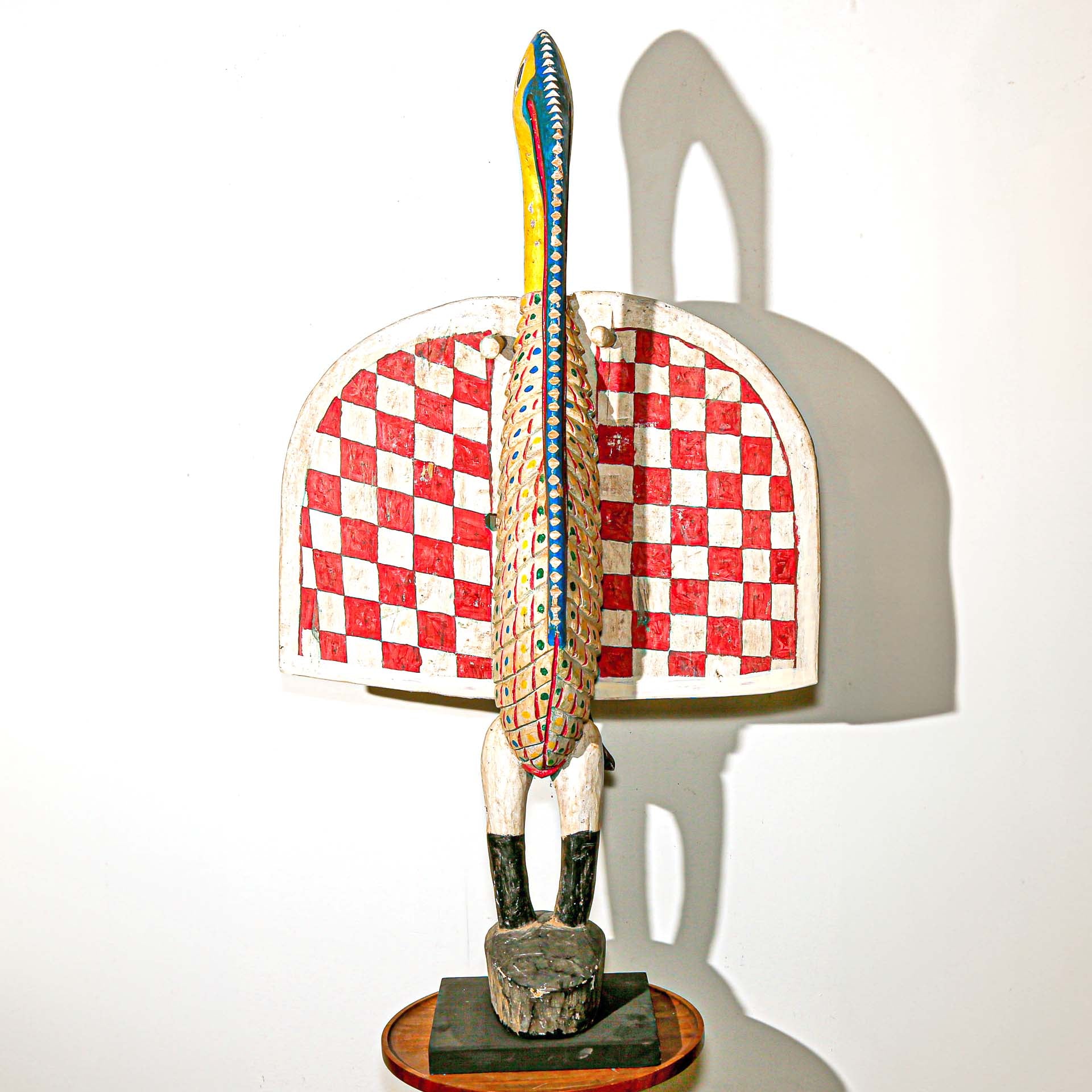 brightly colored wooden sculpture of a large African bird. Red, white, blue, yellow checkered painted designs. 