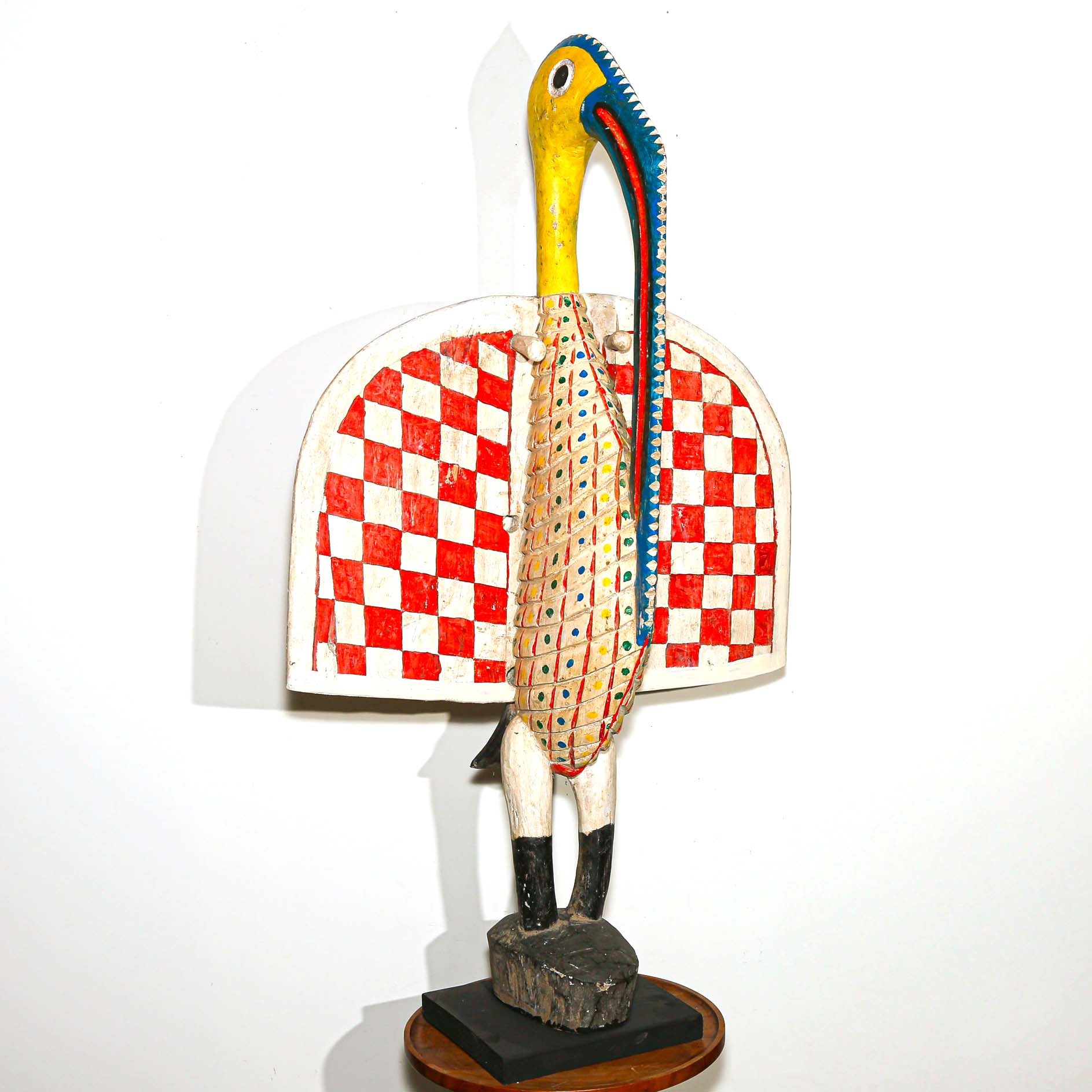 brightly colored wooden sculpture of a large African bird. Red, white, blue, yellow painted designs. 