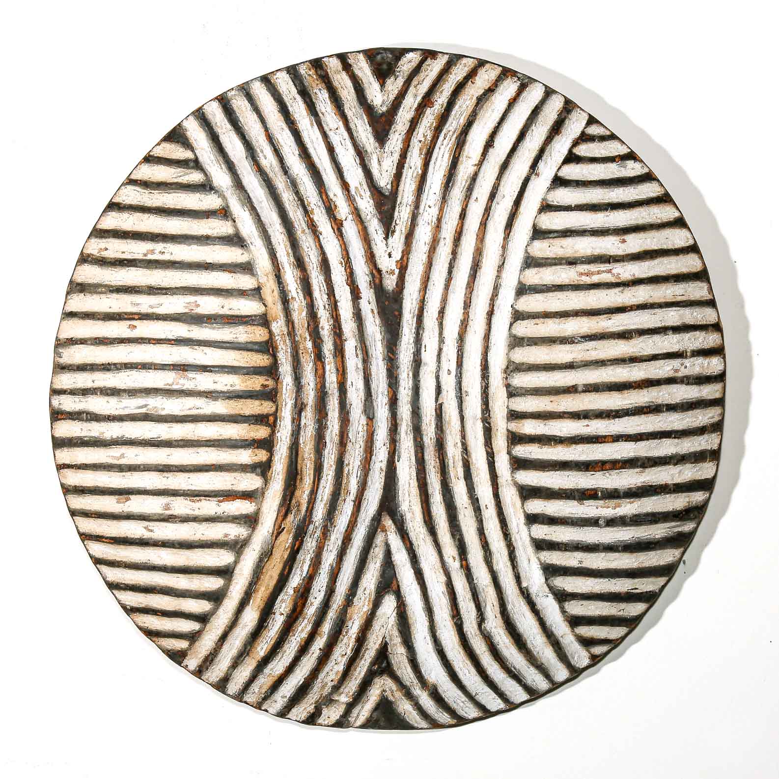 Round wooden wall hanging shield with black and white striped pattern on a white wall