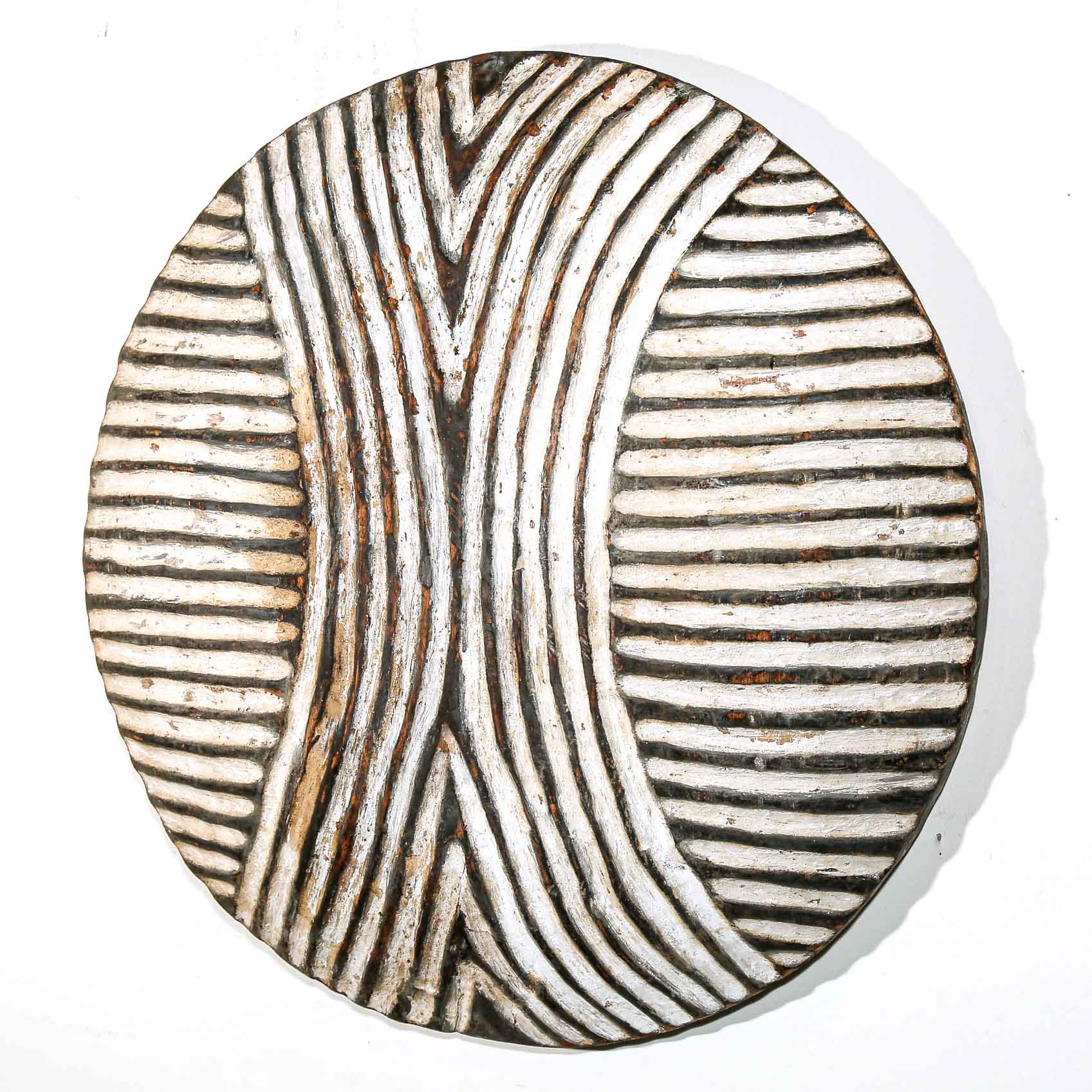 Round wooden wall hanging shield with black and white wavy line pattern on a white wall. 