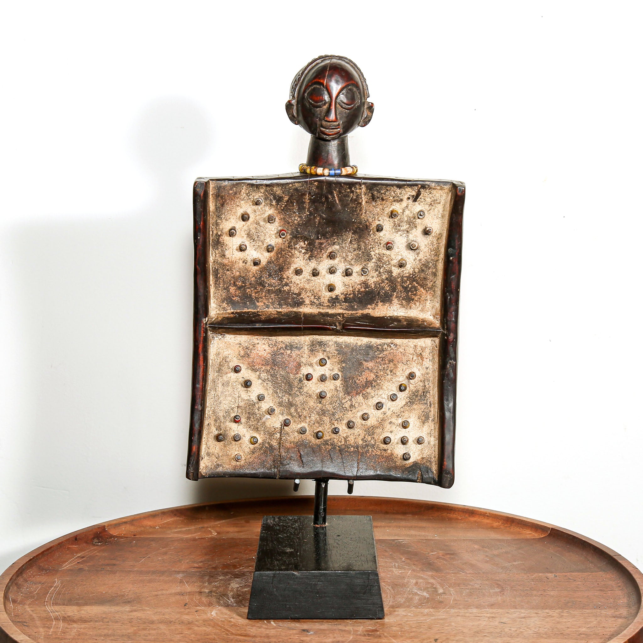 African wooden story telling art with metallic accents on a stand against a white background