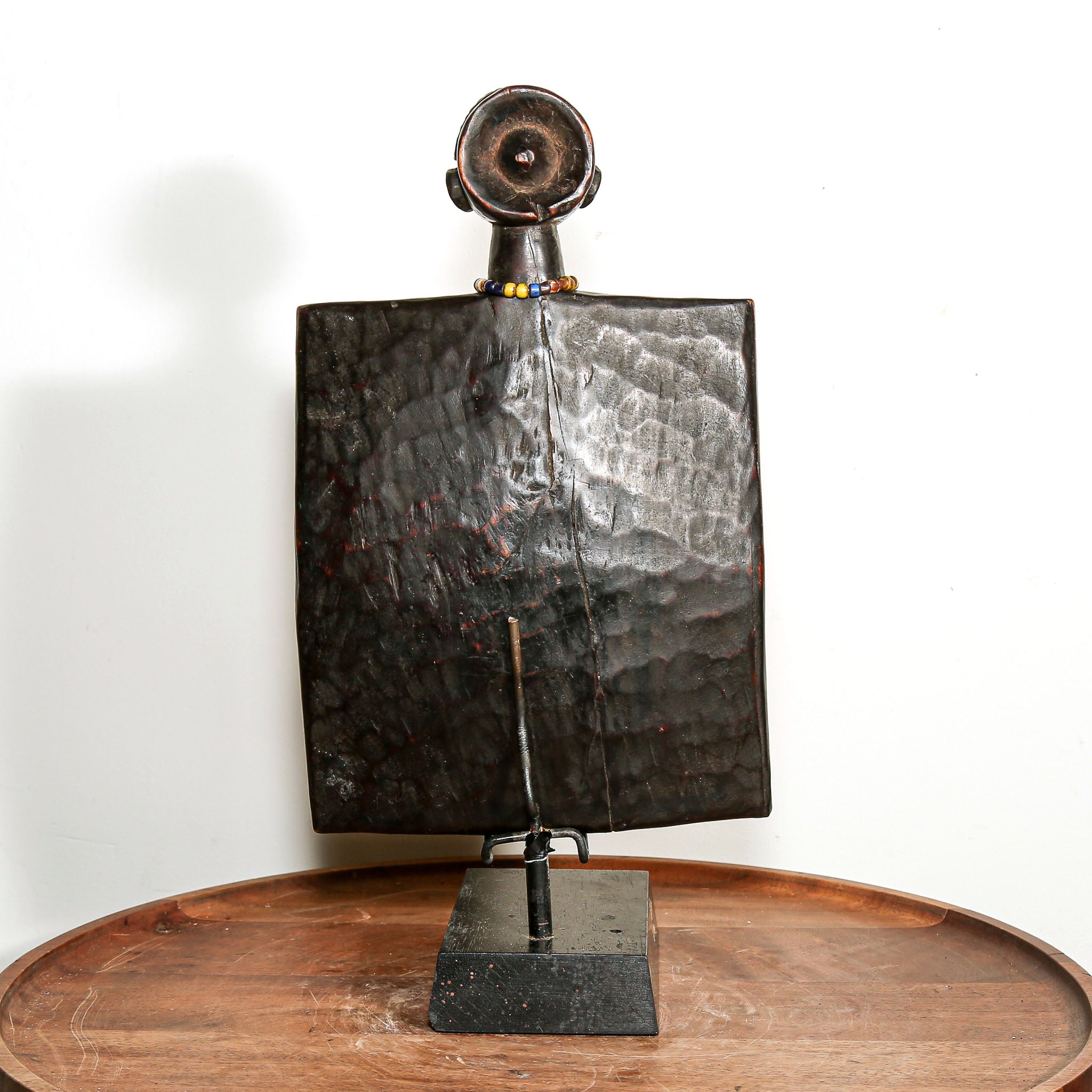 African wooden story telling art with metallic accents on a stand against a white background