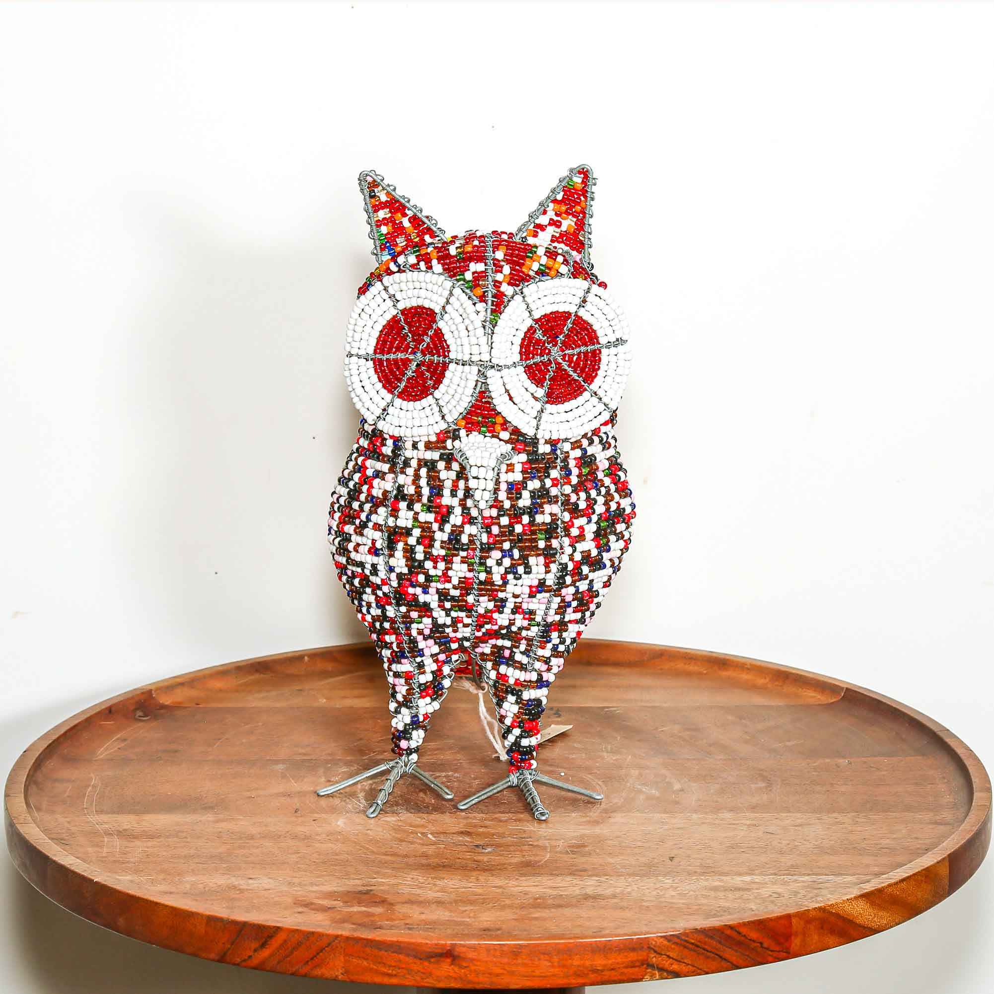 Decorative owl sculpture made out of colored beads from Africa on a wooden table with a white background.