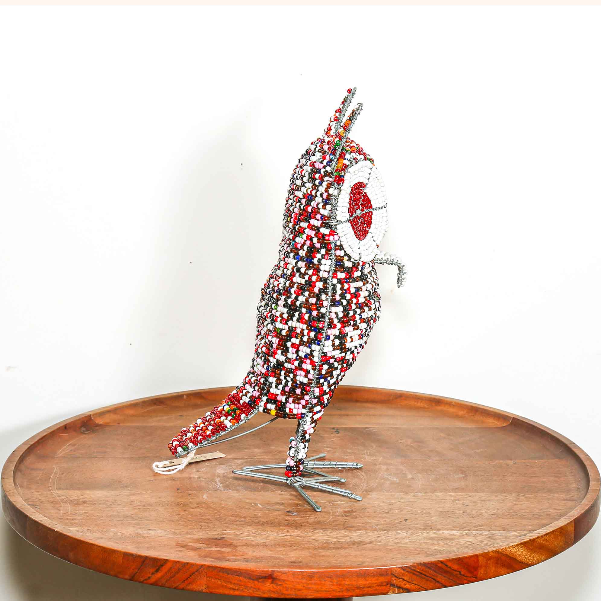 Decorative owl sculpture made out of colored beads from Africa on a wooden table with a white background.