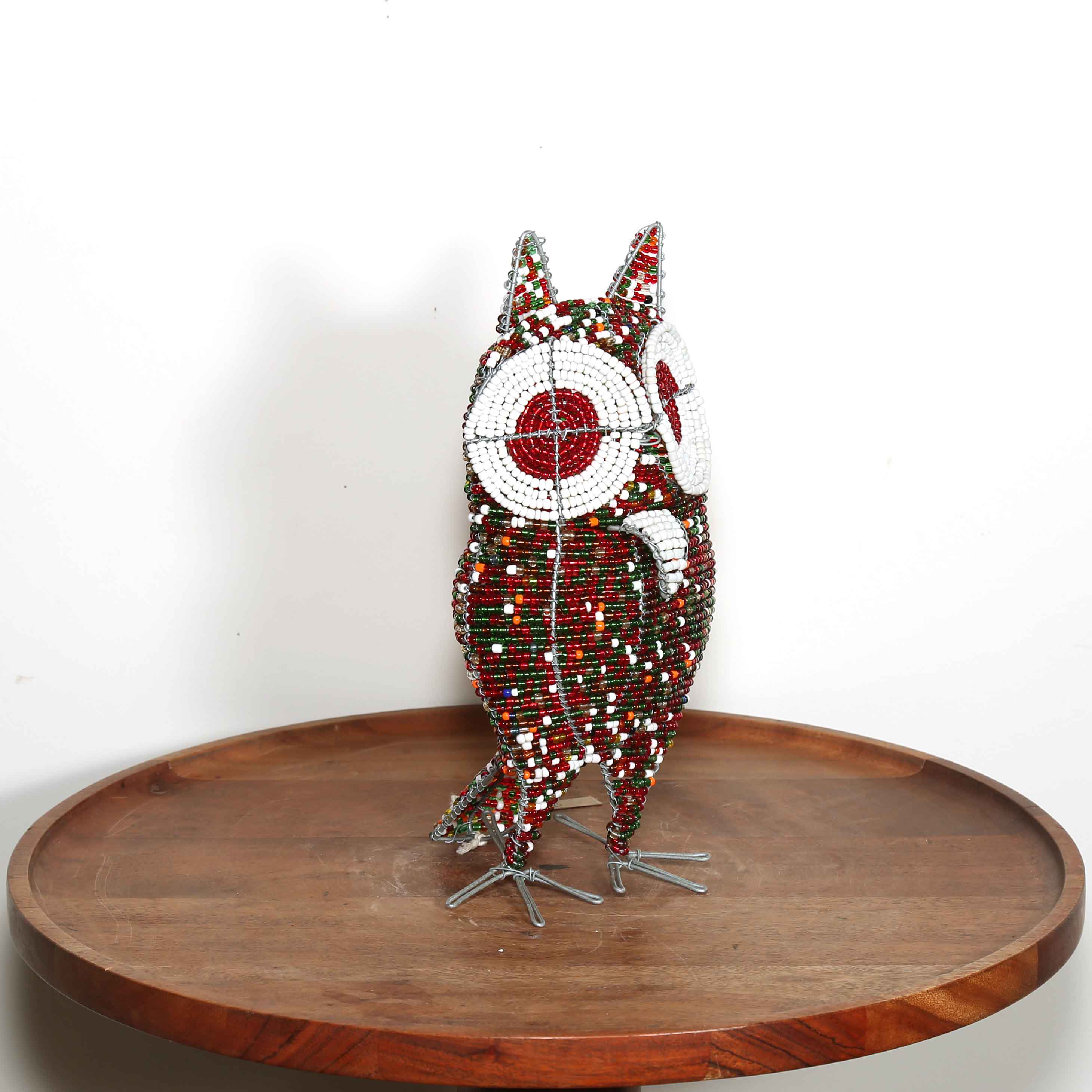 Decorative owl sculpture made out of colored beads from Africa on a wooden table with a white background.