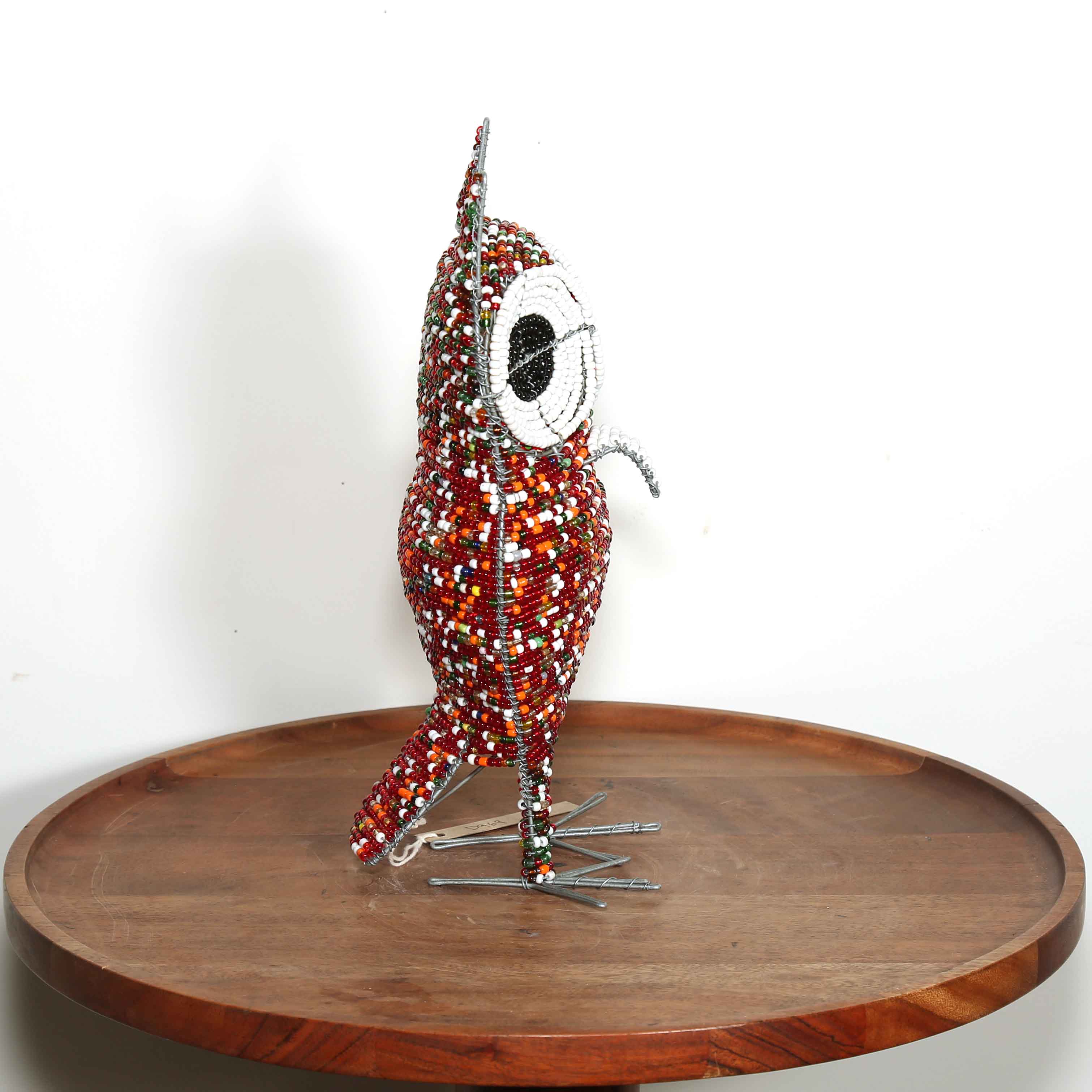 Decorative owl sculpture made out of colored beads from Africa on a wooden table with a white background.