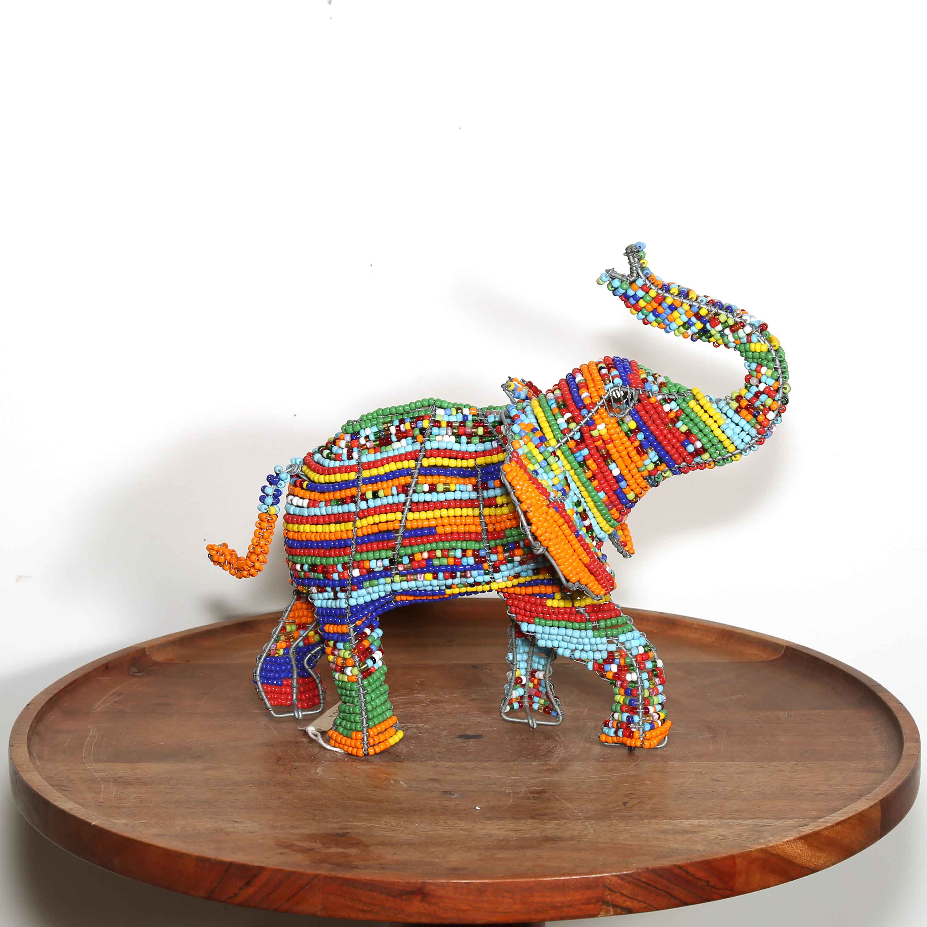 Colorful beaded elephant sculpture on a wooden platform against a white background