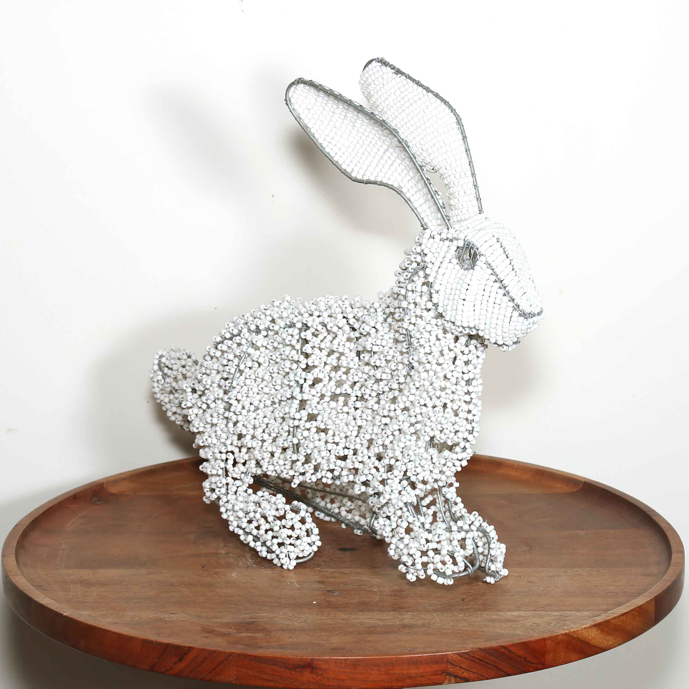 Decorative rabbit sculpture made of small beads on a wooden platform with a white background