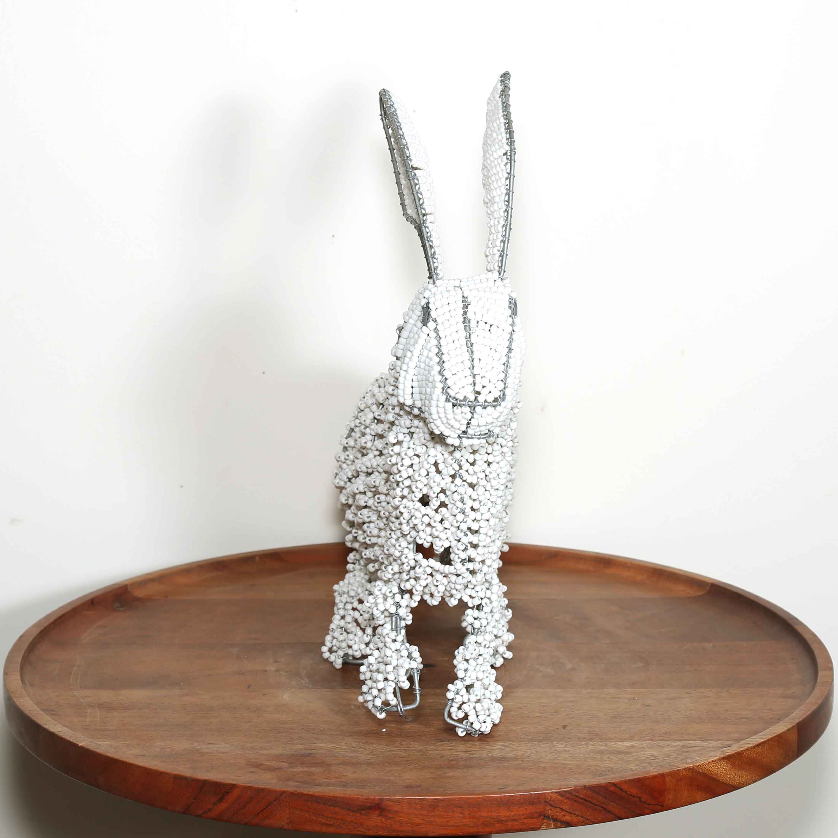 Decorative rabbit sculpture made of interwoven silver wires on a wooden tray with a white background hand-beaded by an African artist