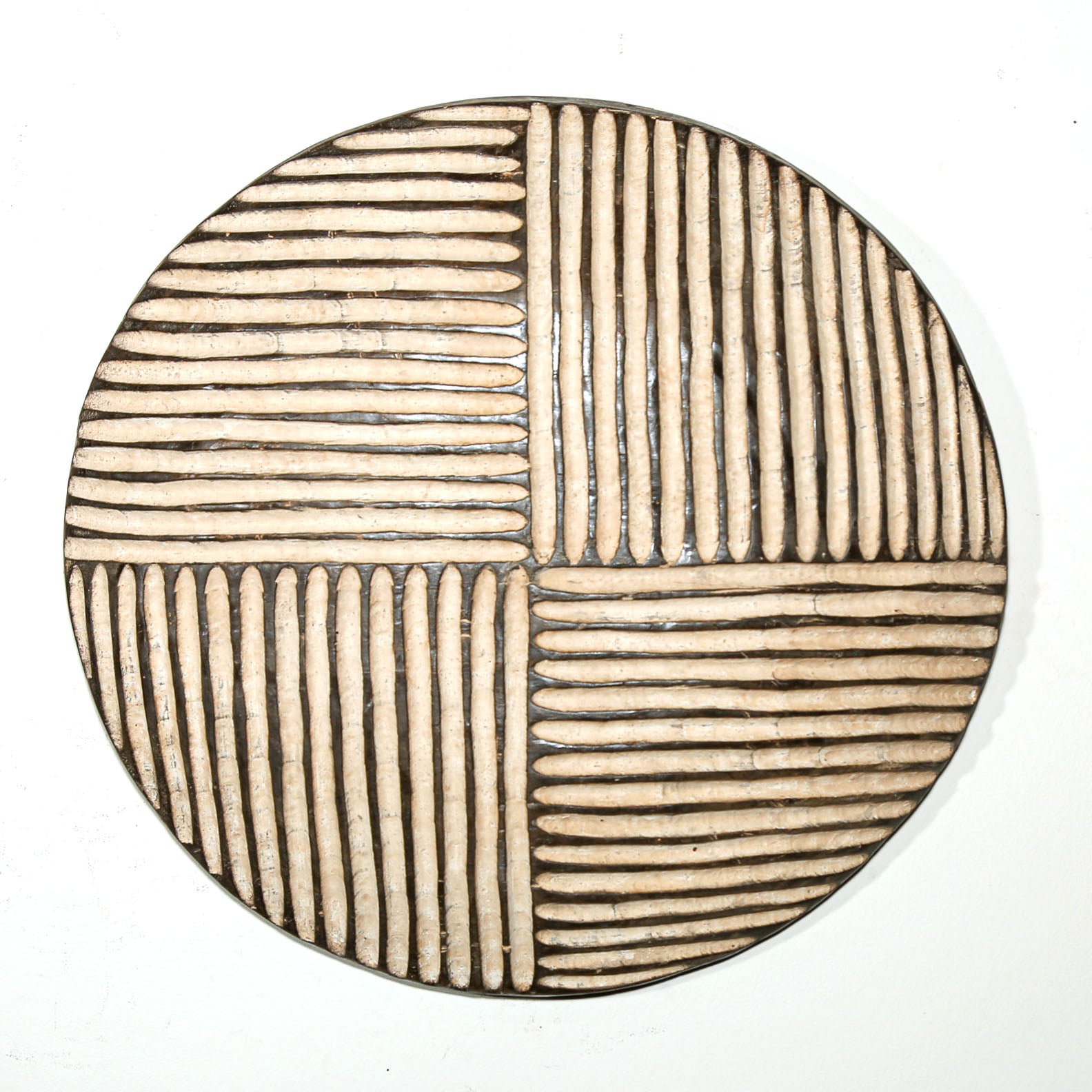 Round wood wall decor with rustic African traditional striped pattern on a white living room wall