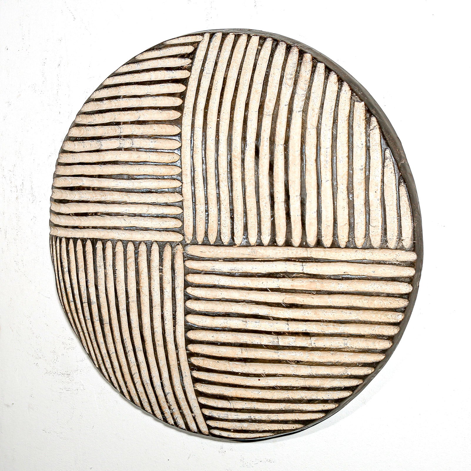 Round wood wall decor with rustic African traditional striped pattern on a white living room wall