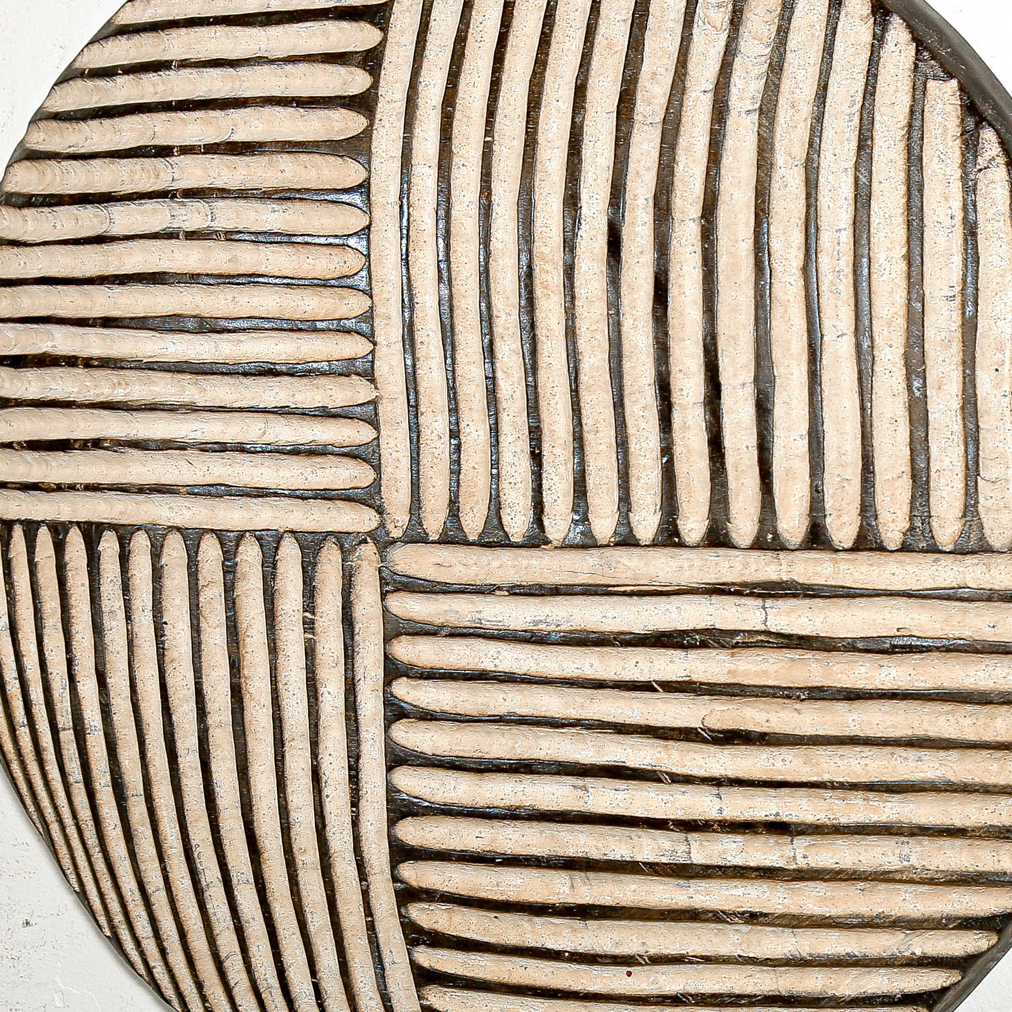 Round wood wall decor with rustic African traditional striped pattern on a white living room wall