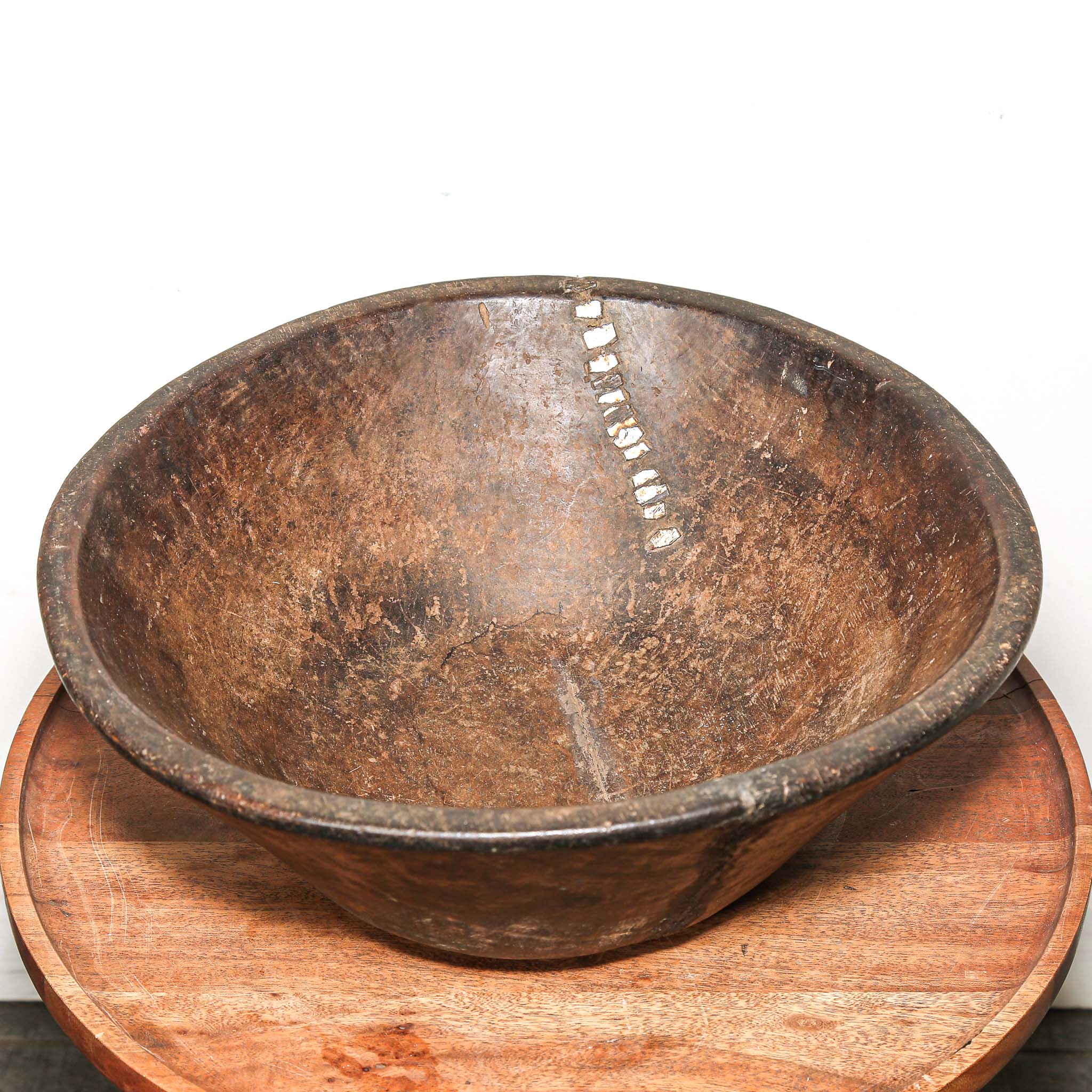 Rustic round Wooden bowl from vintage home decor from Africa on a wooden stand against a white background