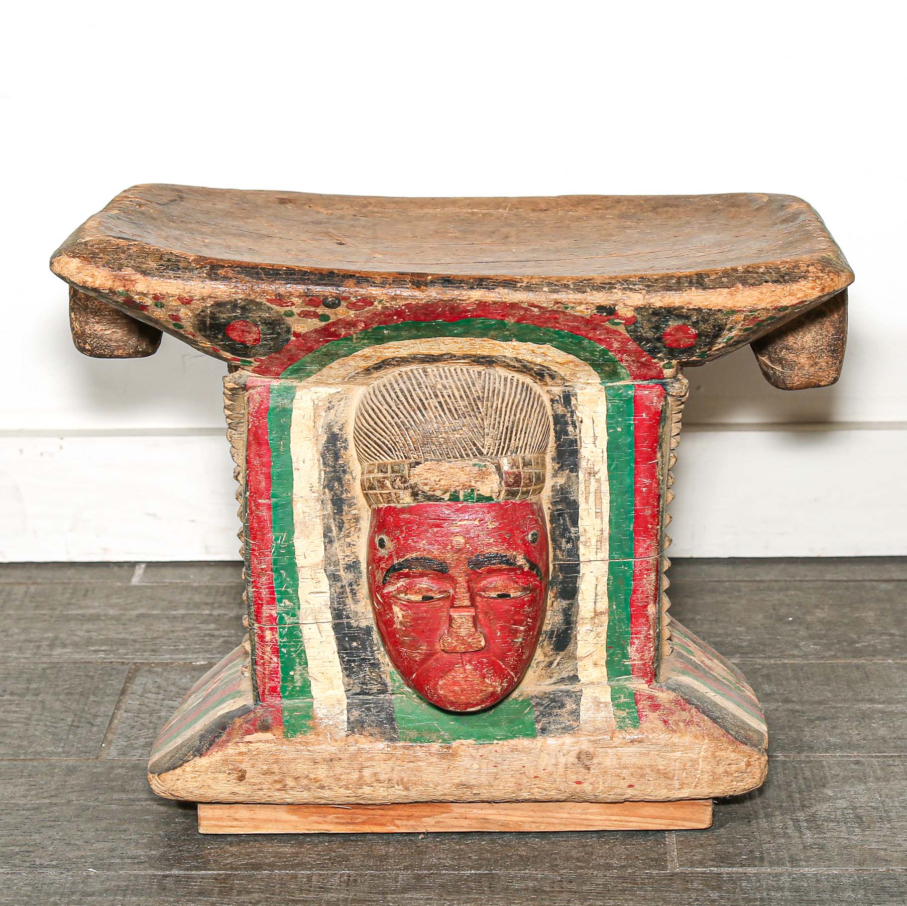 Wooden African stool with a red face design on a white background