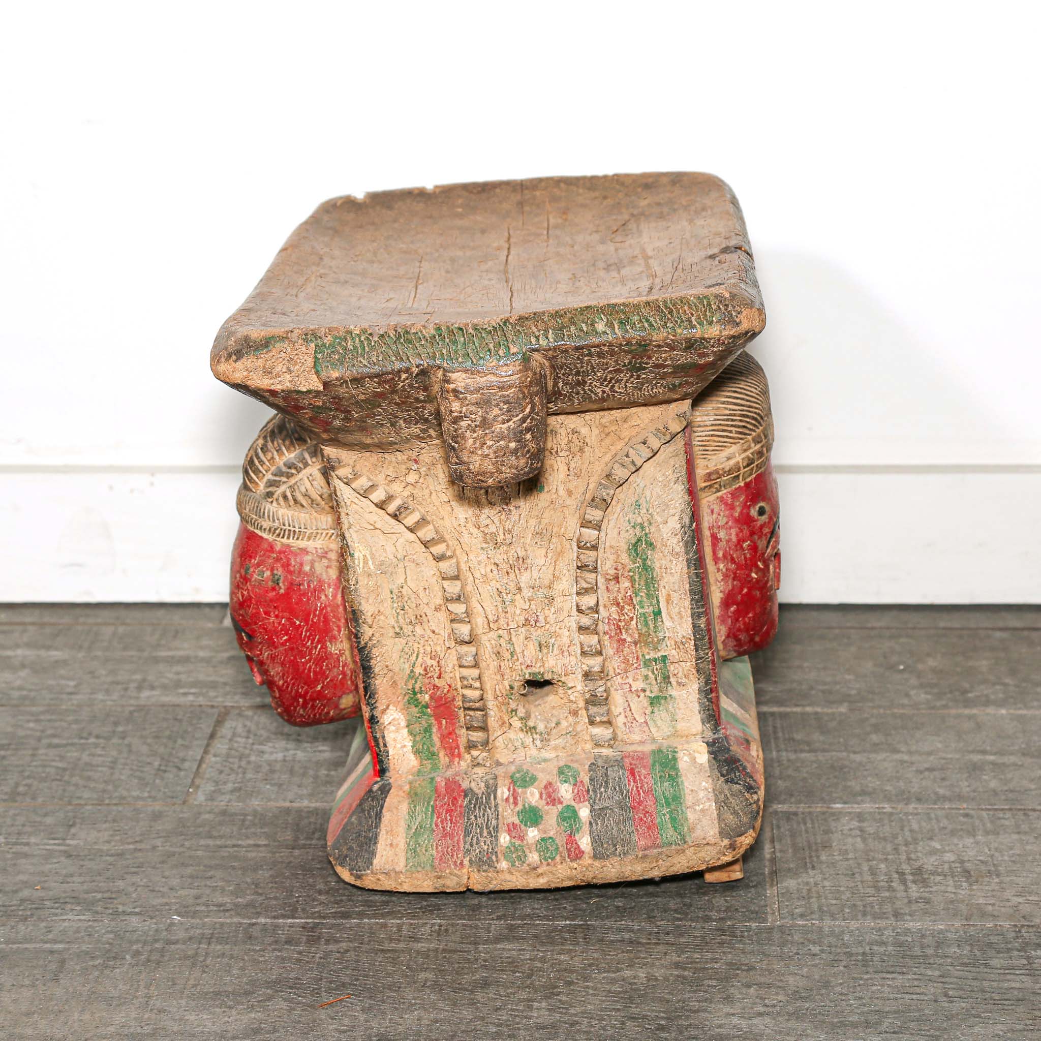 Wooden African stool with a red face design on a white background