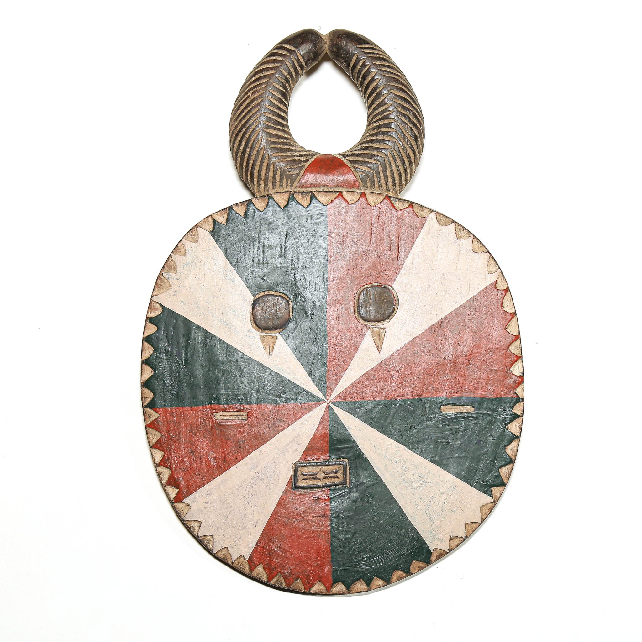 A hand-carved African wooden mask with a circular face, hand-painted in red, green, and beige, and featuring a curved horn-like handle on top, shown against a plain white background.