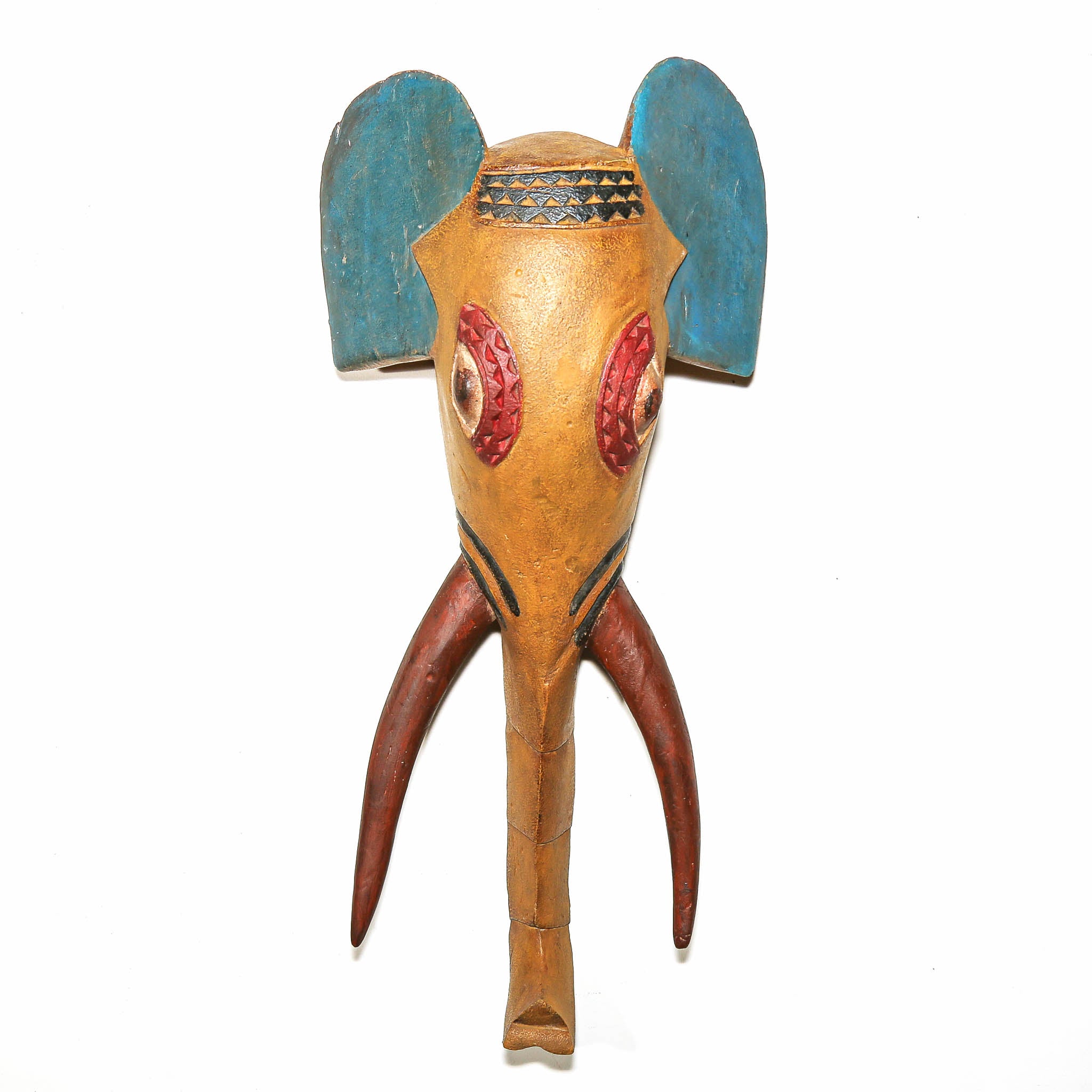 A handcrafted wooden elephant head mask or decorative sculpture with a natural tan wood body, blue ears, red eye details, and brown tusks, shown against a plain white background.