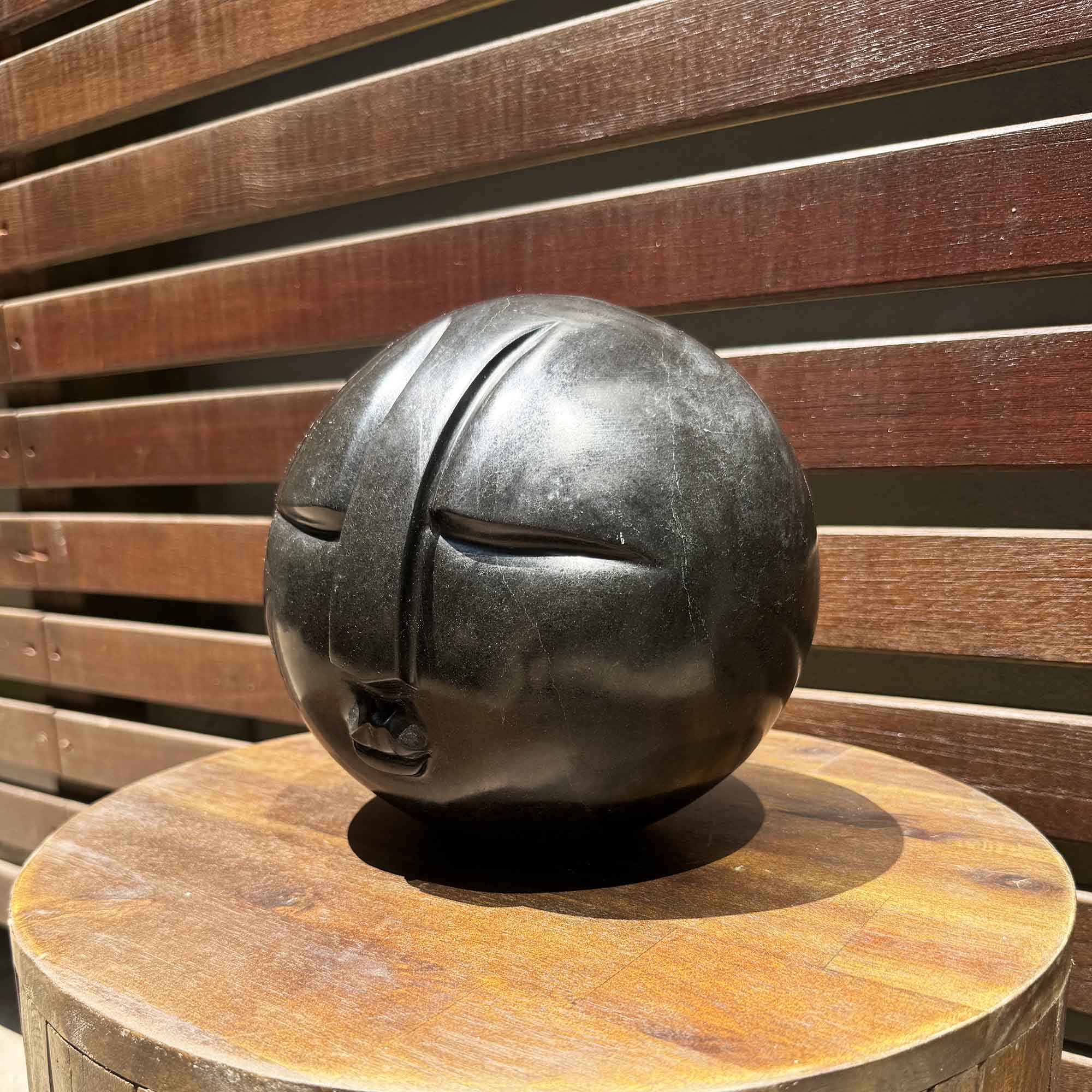 Decorative black sphere with a face on a wooden stool against a wooden slatted background