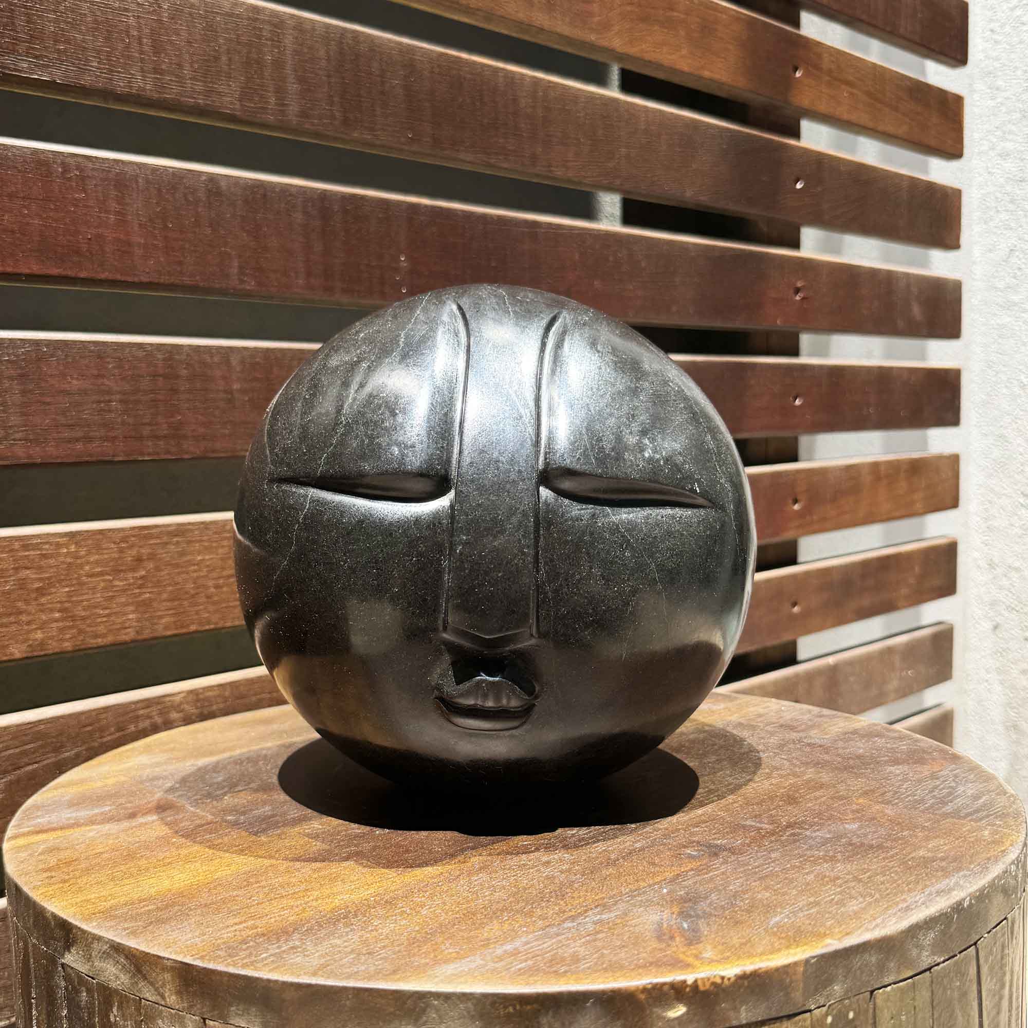 Decorative stone sculpture of a face on a wooden pedestal against a wooden slat background