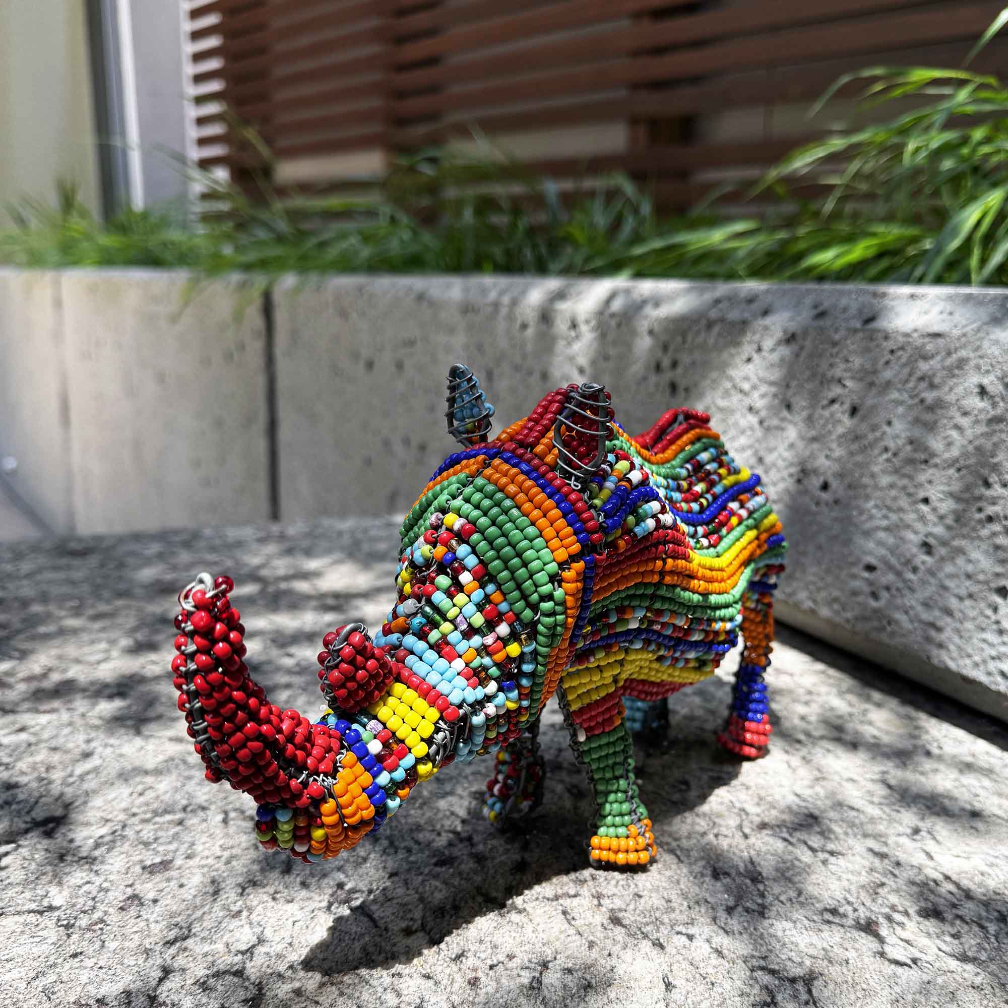 Colorful beaded rhino sculpture on a stone surface with a garden background