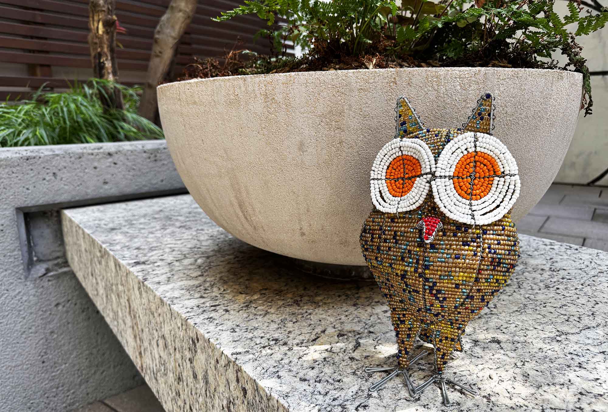 beaded owl sculpture on a stone surface with a planter in the background