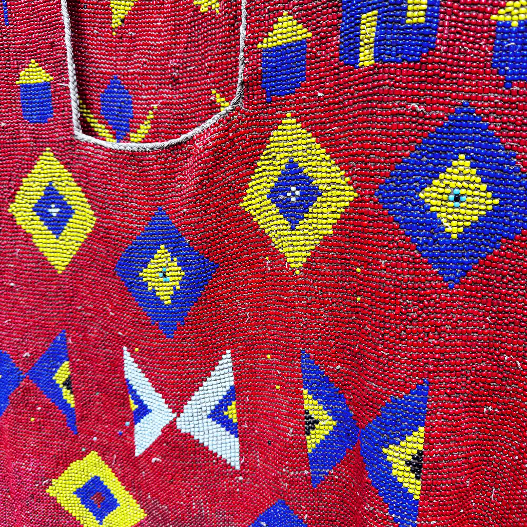 Close-up of a red beaded fabric with blue, yellow, and white geometric patterns. African art for sale