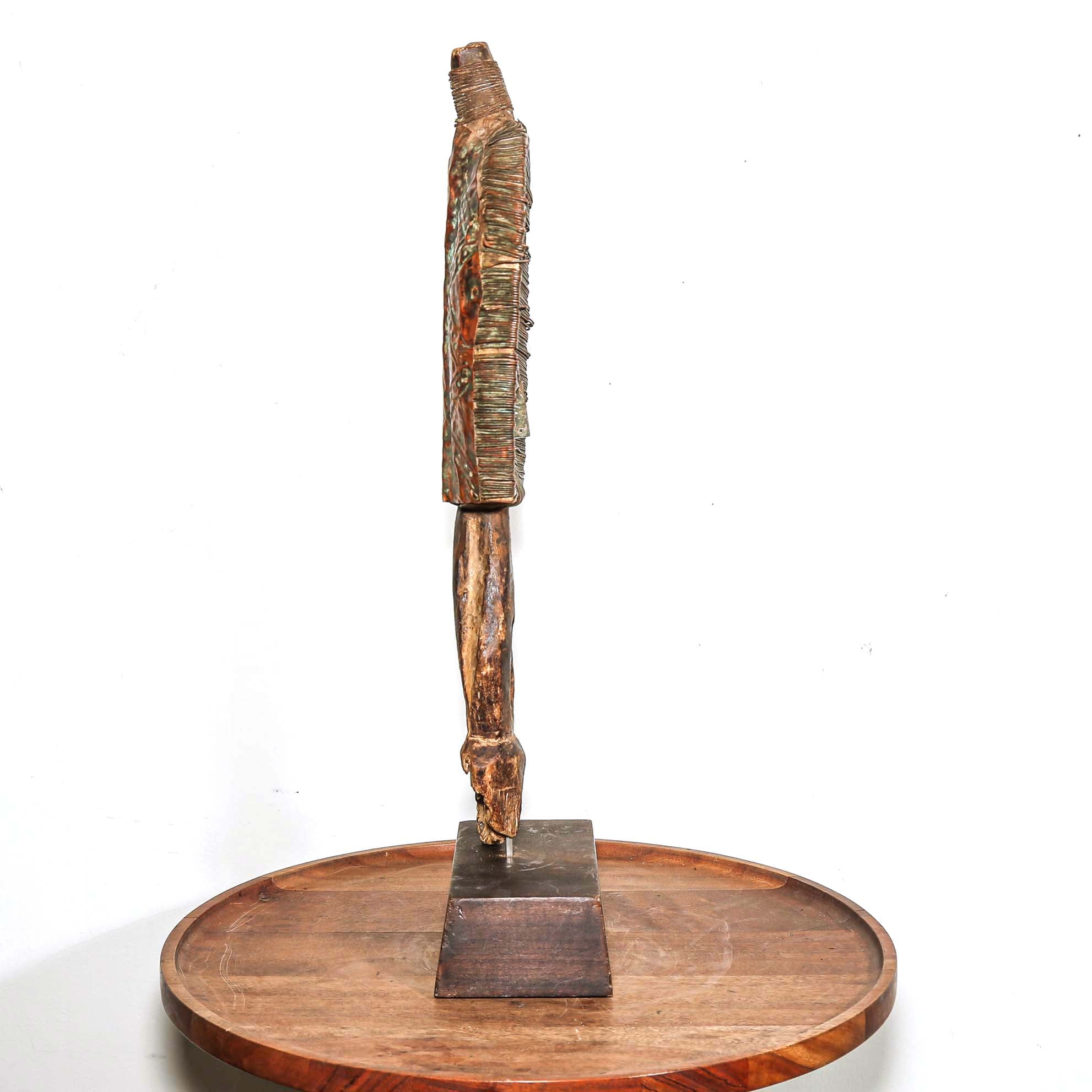 Wooden protective traditional mask from Gabon made from wood and metal on a round wooden table with a white background shown with profile view