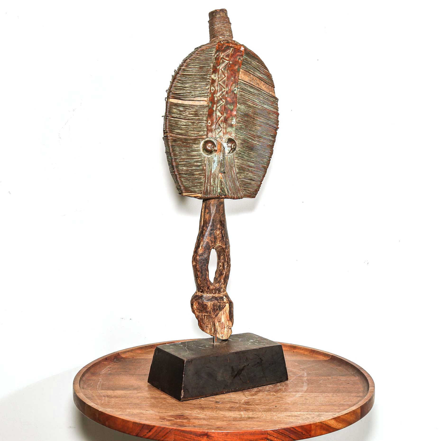 Wooden protective traditional mask from Gabon made from wood and metal on a round wooden table with a white background shown from the side