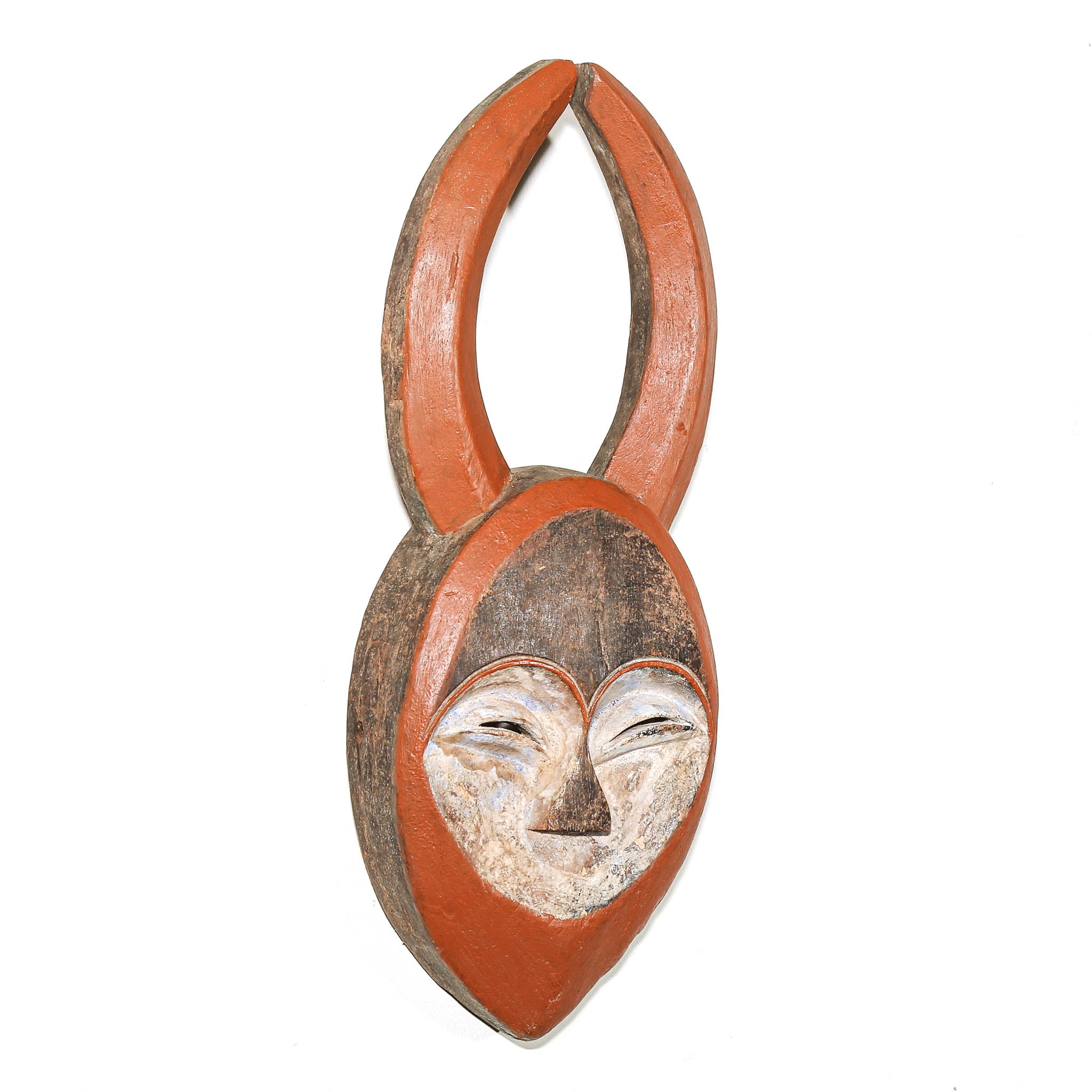 A hand-carved wooden mask with a stylized face and tall curved horns, painted in terracotta orange, brown, and off-white, isolated on a white background.
