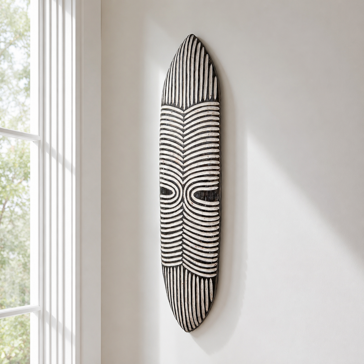 black and white African dancing shield displayed on a white wall near a window with natural light