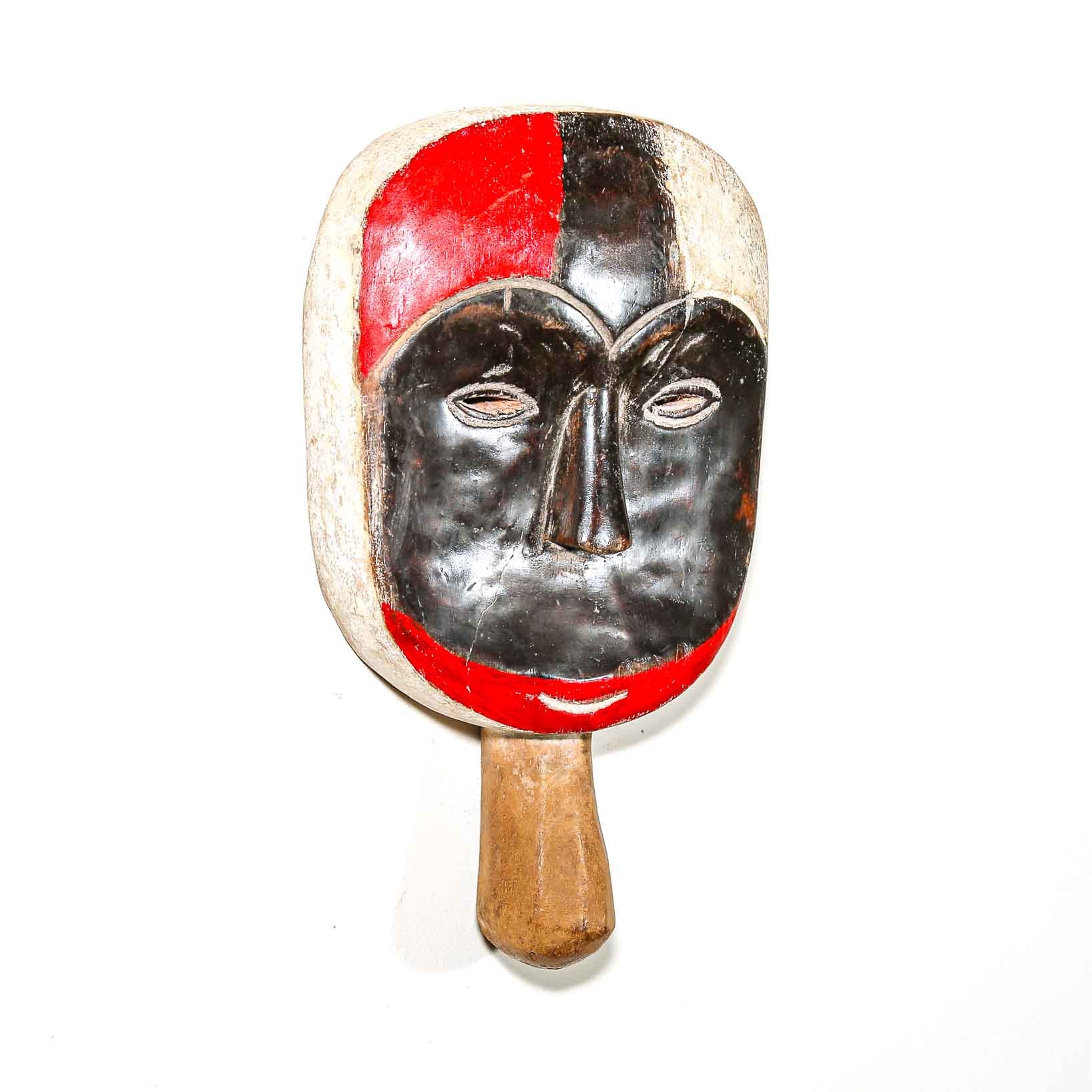 Wooden paddle with a mask design featuring red and black on a white background