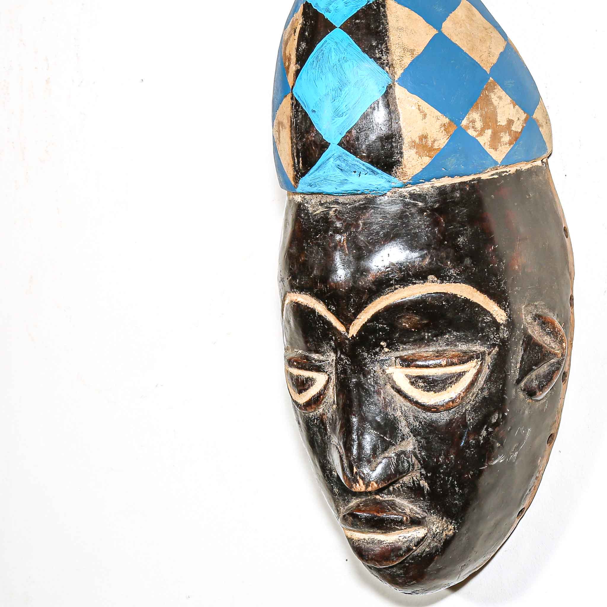 African mask with a checkered blue and gold headdress on a white background