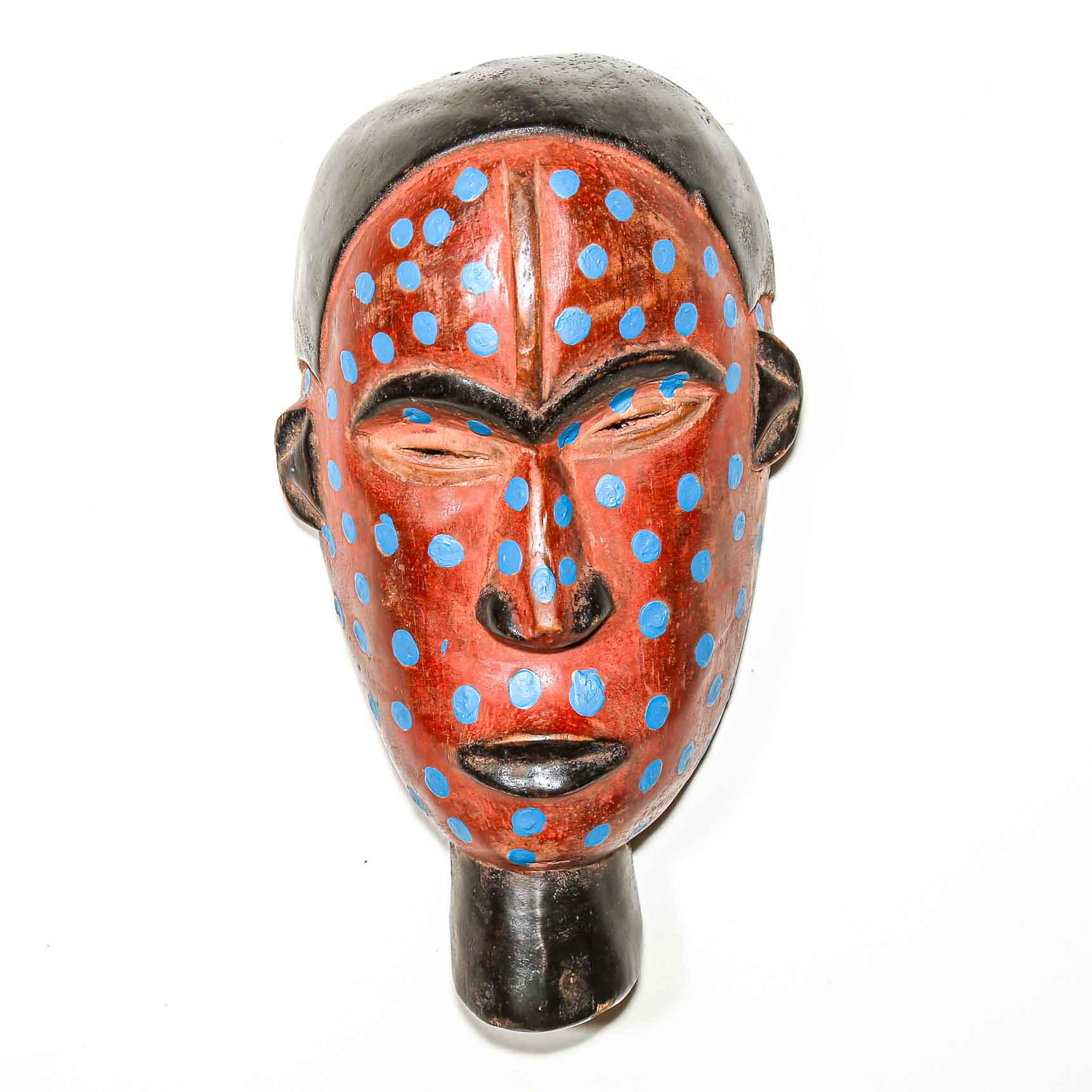 Wooden African mask with red face and blue polka dots on a white background