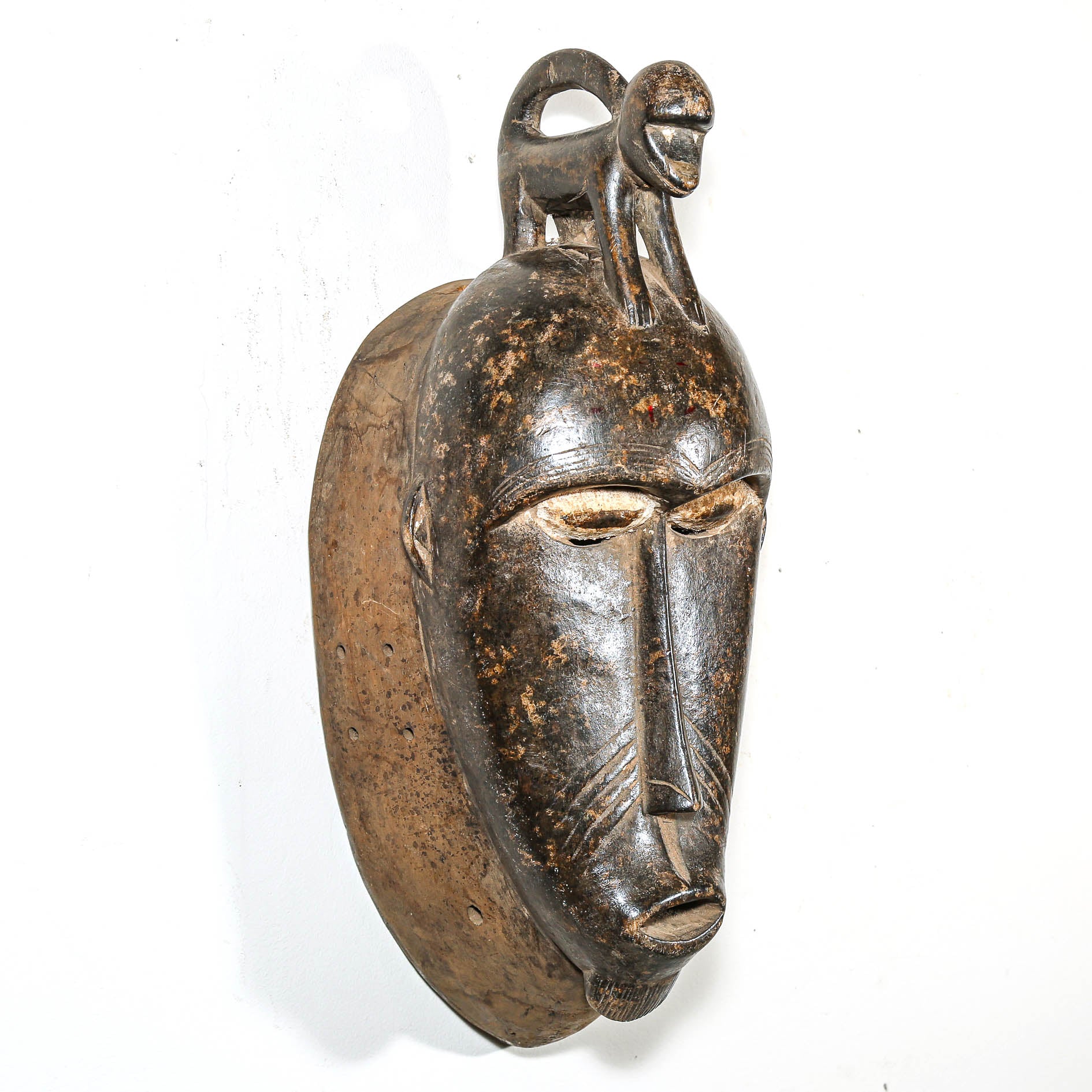 African mask with a detailed face and monkey headdress on a white background
