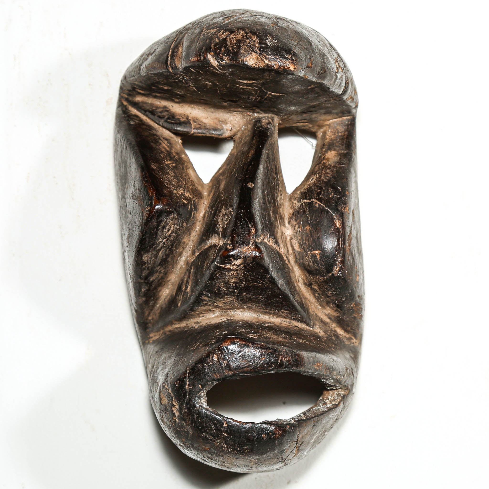 Carved antique tribal ceremonial black wooden mask on a white background