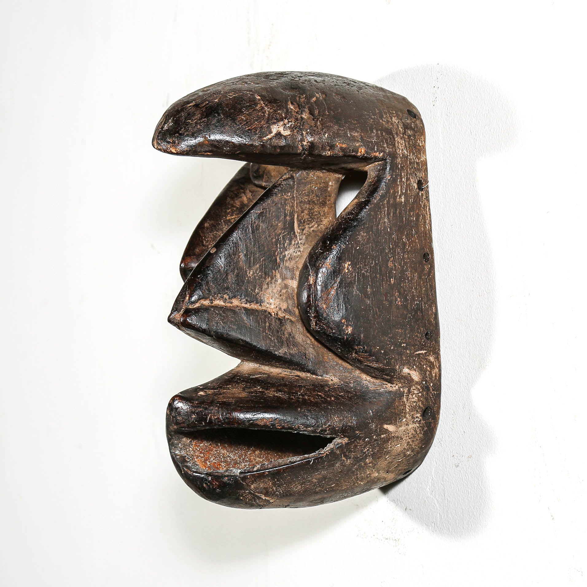 Carved antique tribal ceremonial black wooden mask on a white background