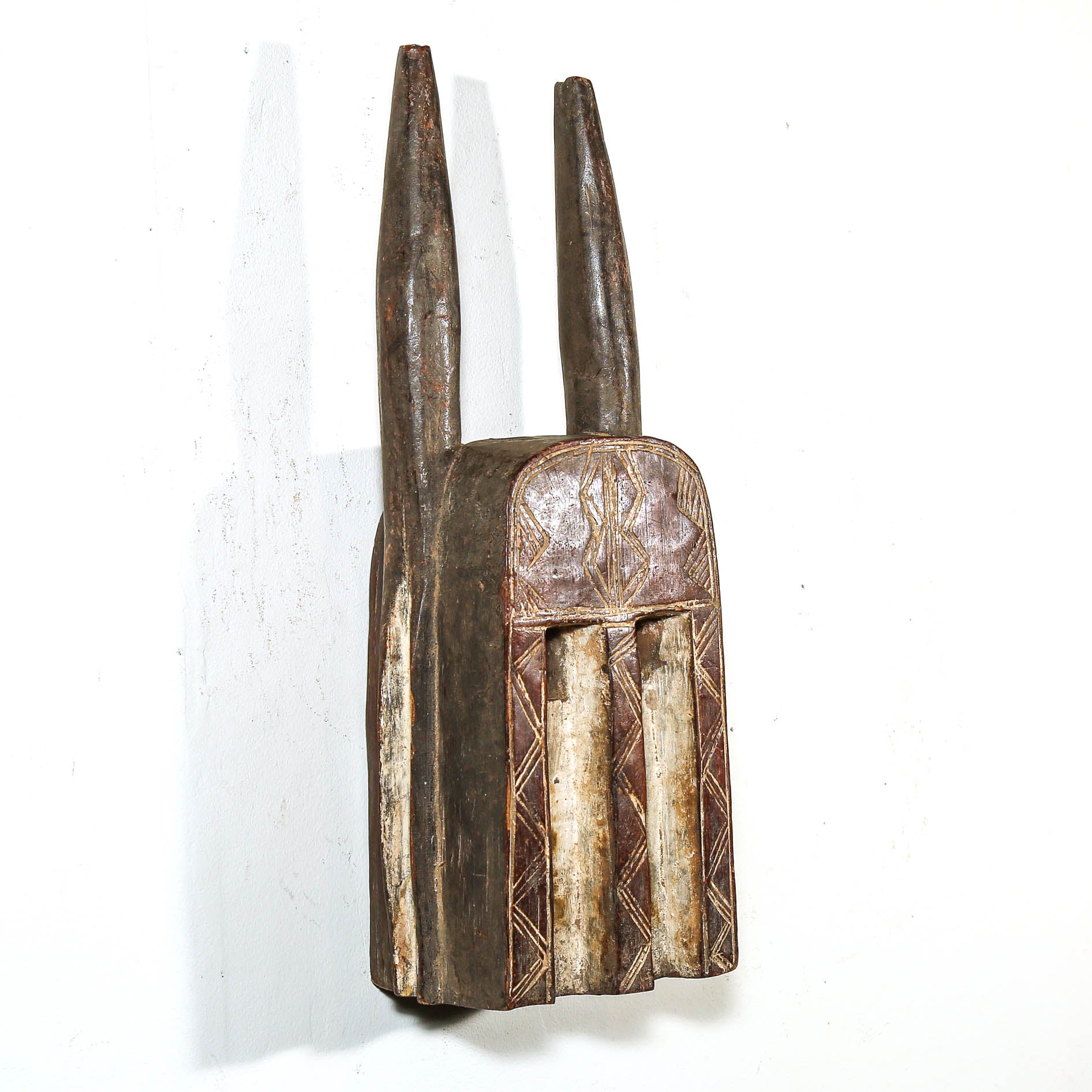 Decorative wooden mask from Mali with long horns on a white background