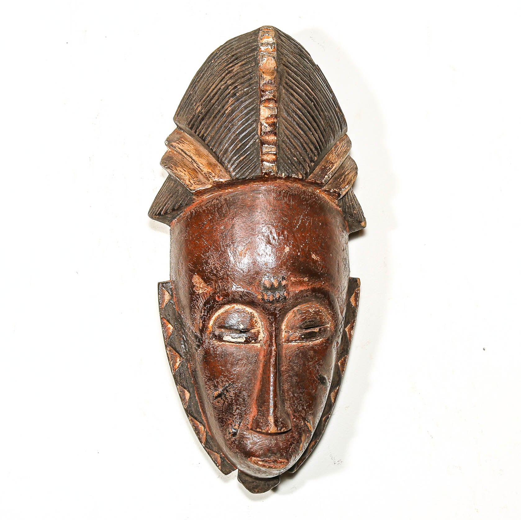 Wooden black African art mask with detailed carvings on a white background