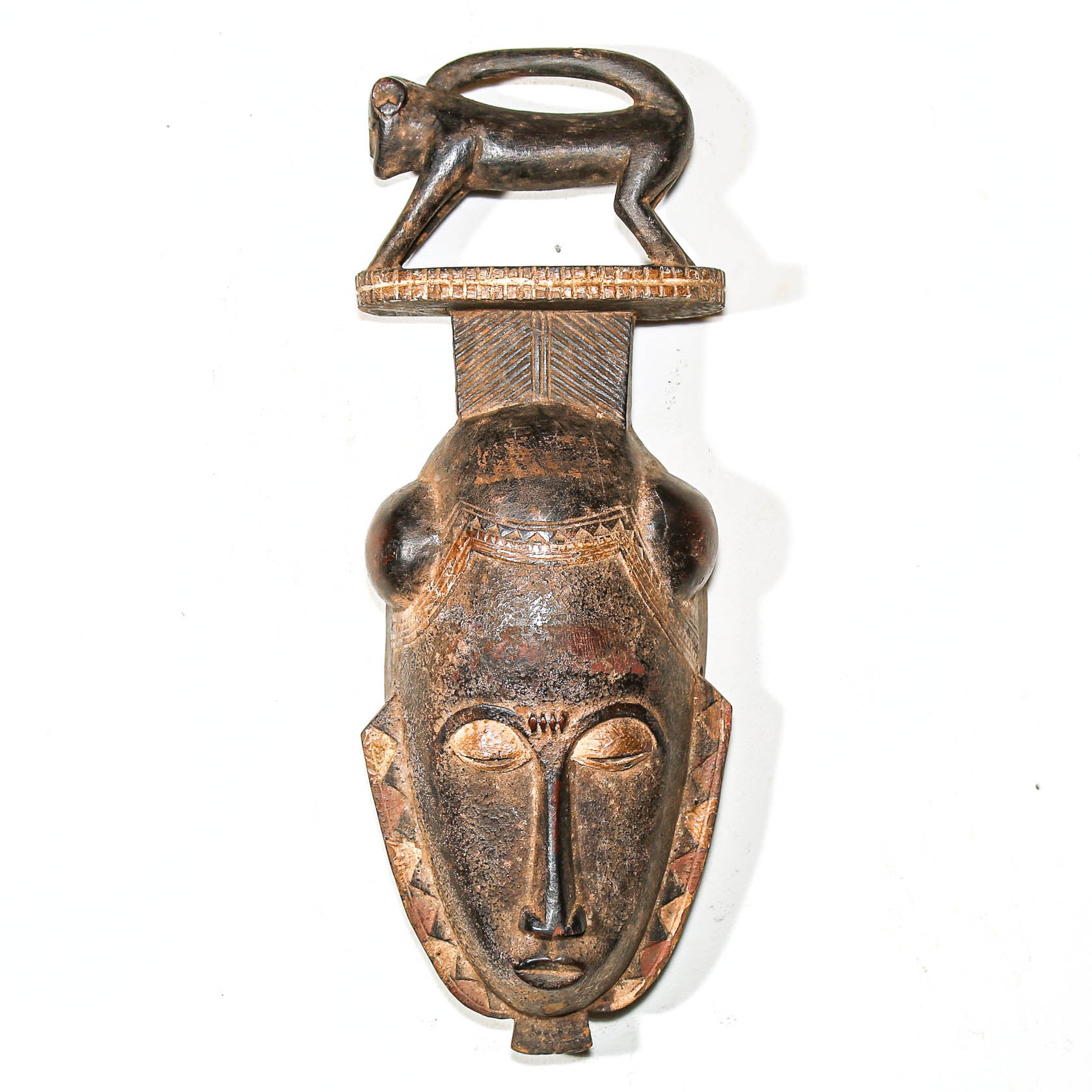 wooden African mask with face and small figure on top against a white background