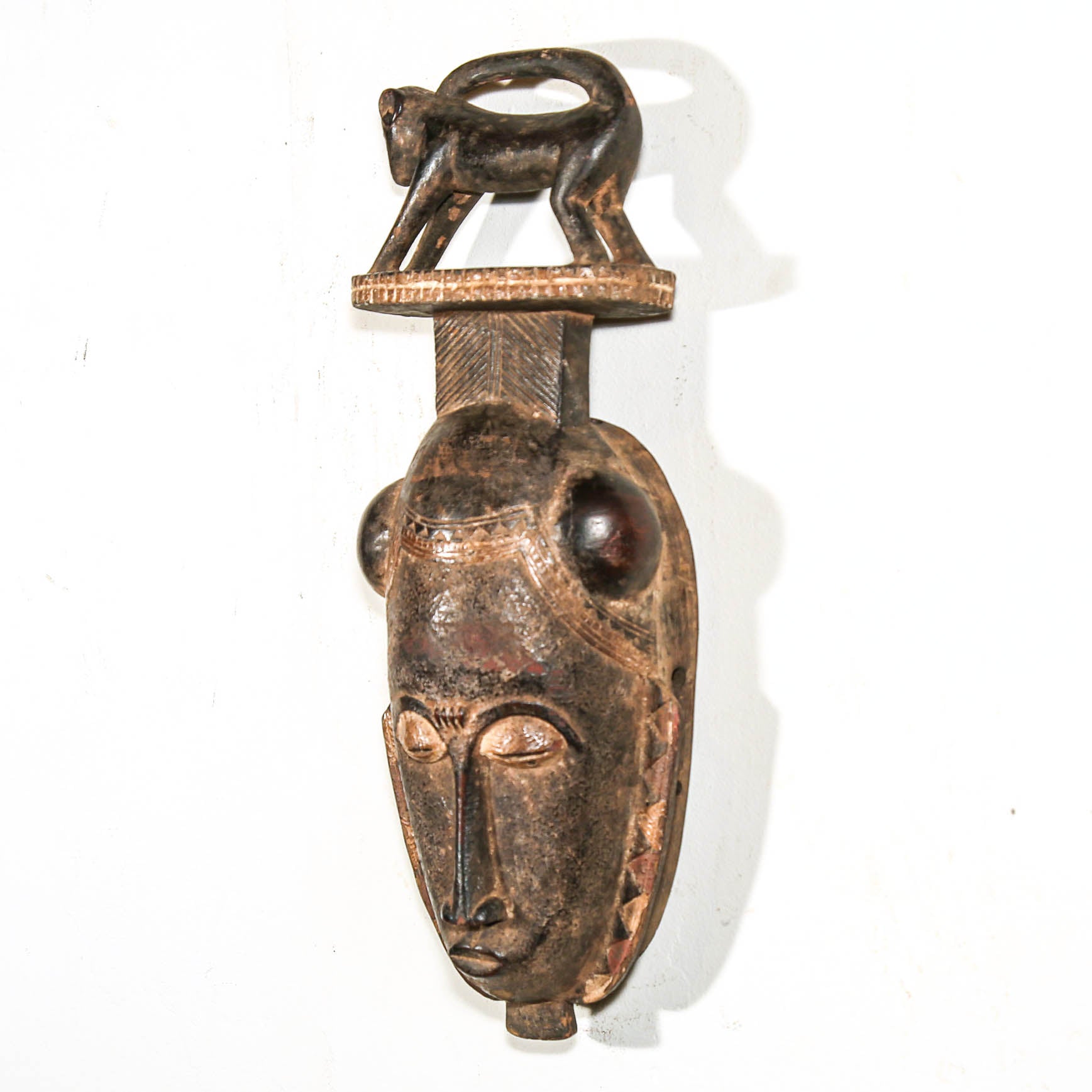 wooden African mask with face and animal figure on top against a white background