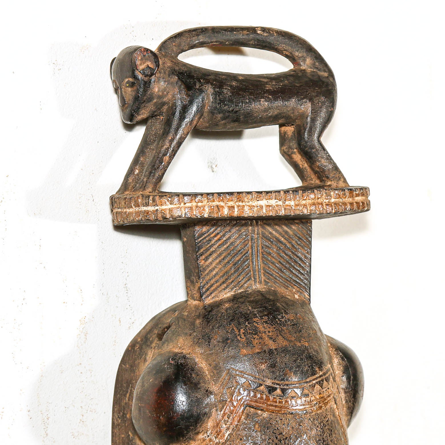 wooden African mask with face and small figure on top against a white background