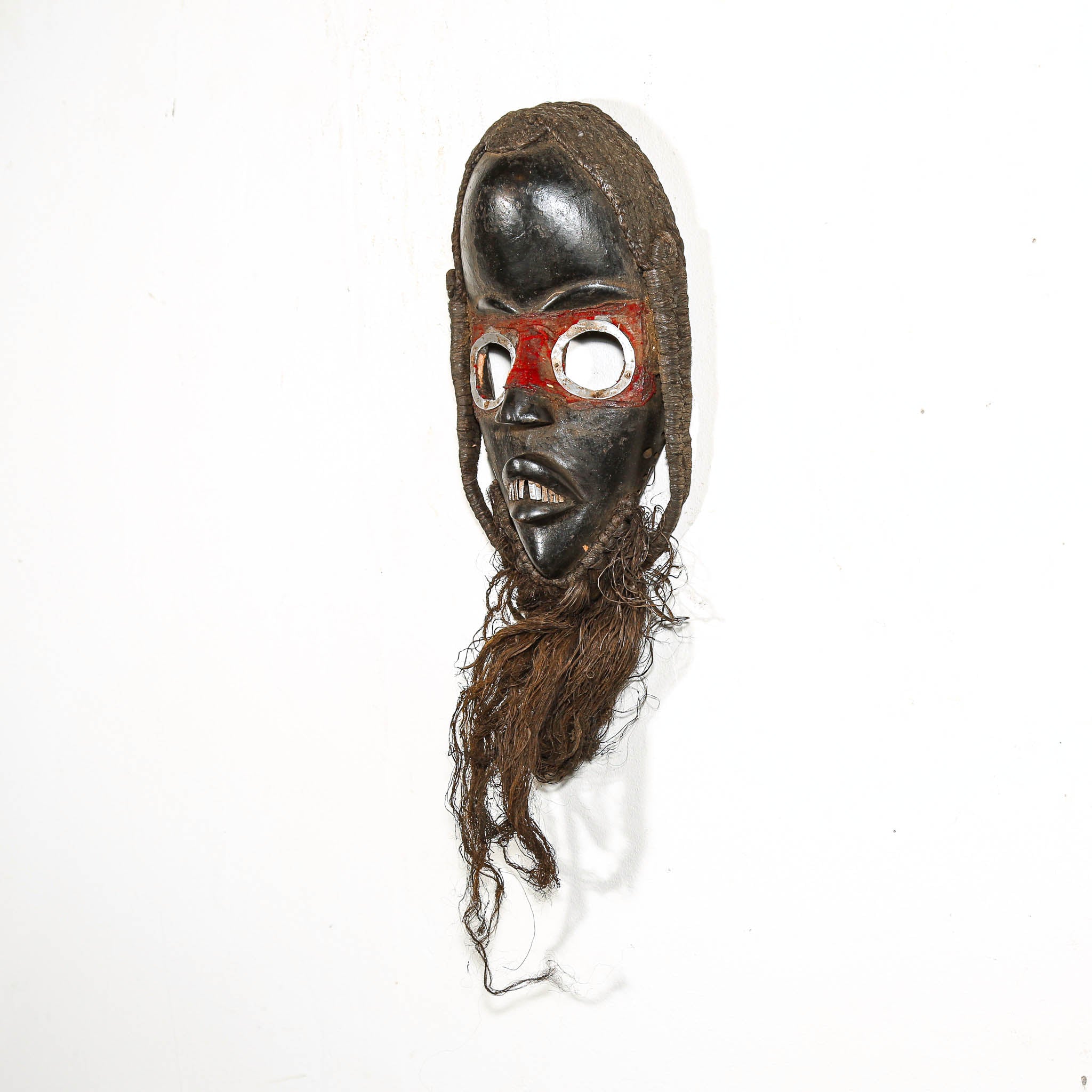 Traditional mask with red eyes and braided hair on a white background from Africa for sale