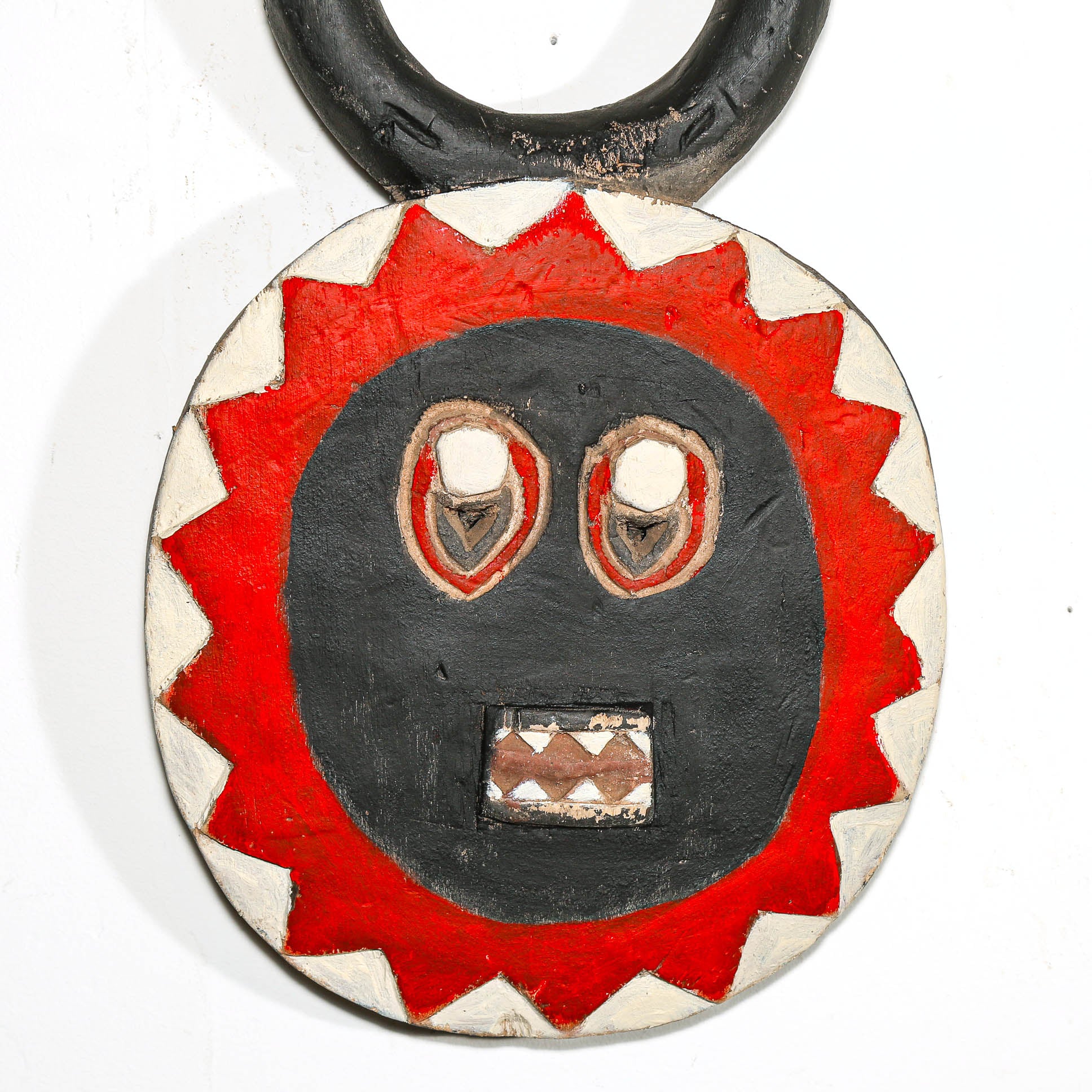 Round wooden African mask with a red and black face design on a white background